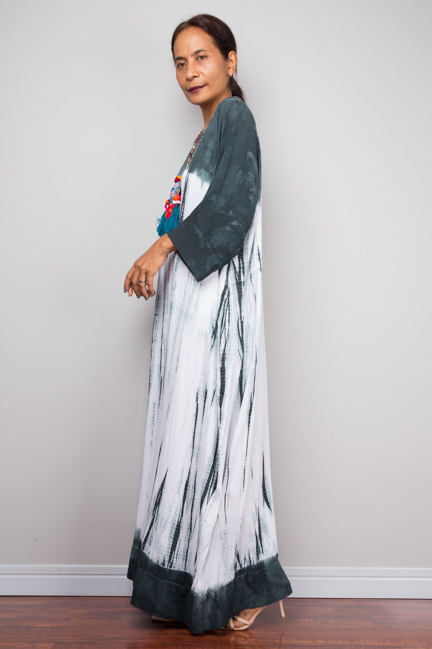 Woman wearing a long, patterned shibori tie dye maxi dress with a plain background