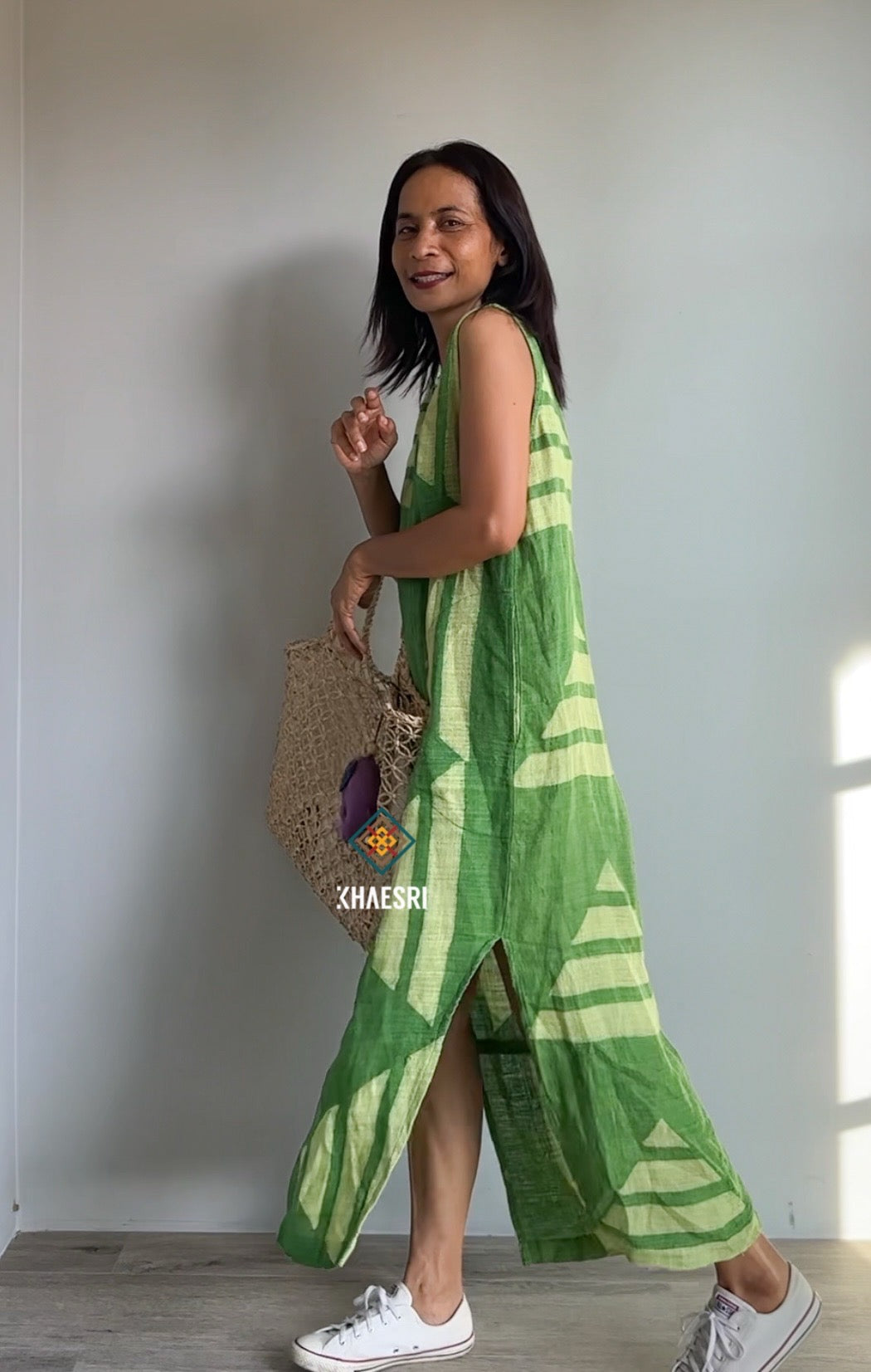 Model in a Nuichan sleeveless hemp kaftan dress, featuring a handwoven green geometric design with white accents. This boho dress, perfect for summer or tropical climates, is captured indoors with white sneakers for a fresh look.