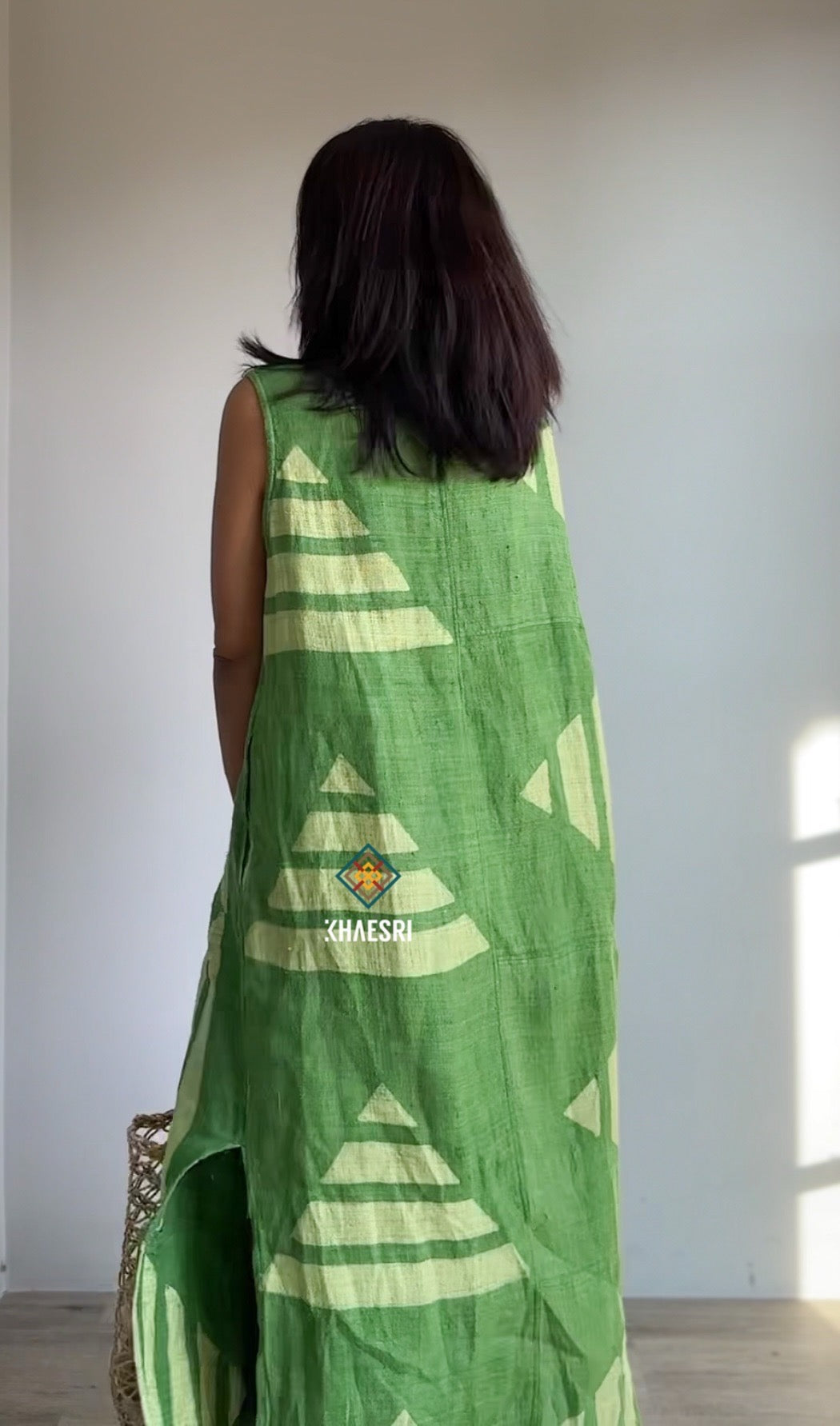 Nuichan sleeveless kaftan dress made from handwoven hemp, featuring a green geometric pattern with side slits. This loose-fit boho dress, photographed indoors, offers breathable comfort for warm weather with a relaxed silhouette.