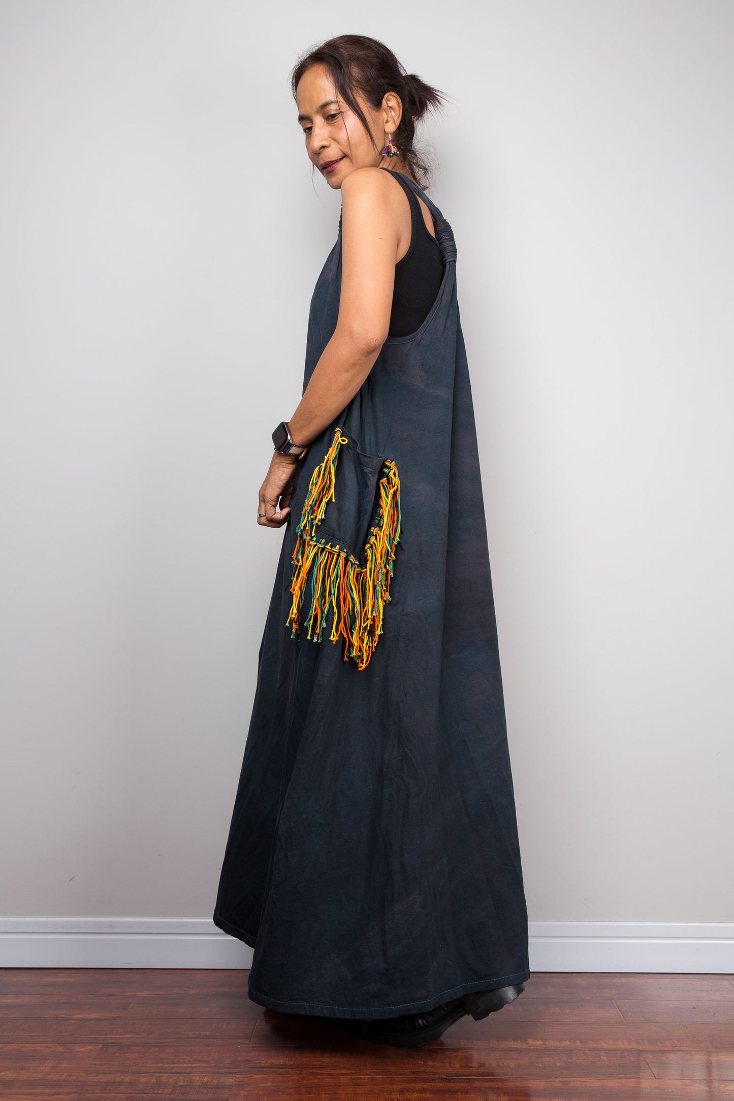 Side view of a model wearing the Nuichan sleeveless tie-dye boho maxi dress, showing the scoop neckline, flowing A-line silhouette, and a multicolour yarn fringe patch pocket on the hip.