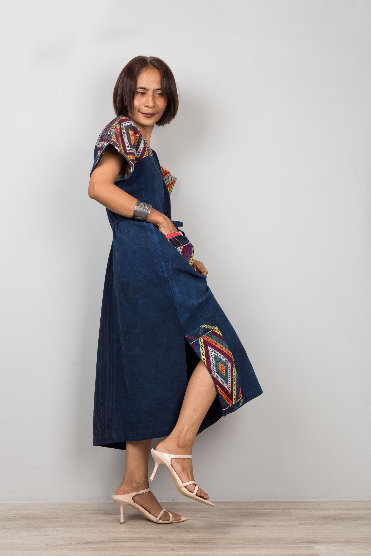 Woman wearing a blue dress with colorful embroidered patterns on a plain background