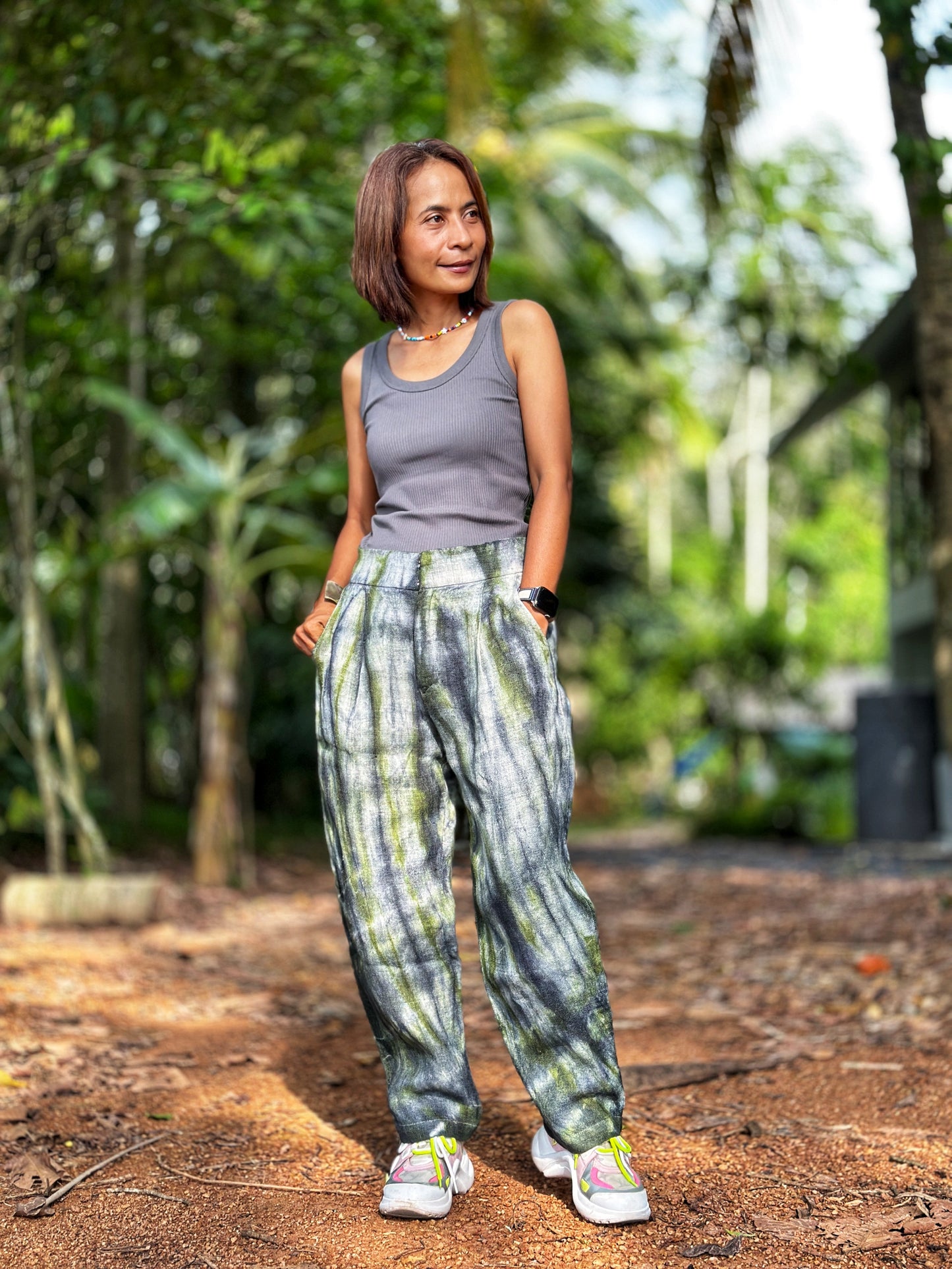 Model wearing Nuichan tie-dye hemp pants in a gray-green shade, crafted from handwoven Hmong hill tribe fabric. These boho hemp trousers, with their loose fit and four pockets, are styled with a simple top.