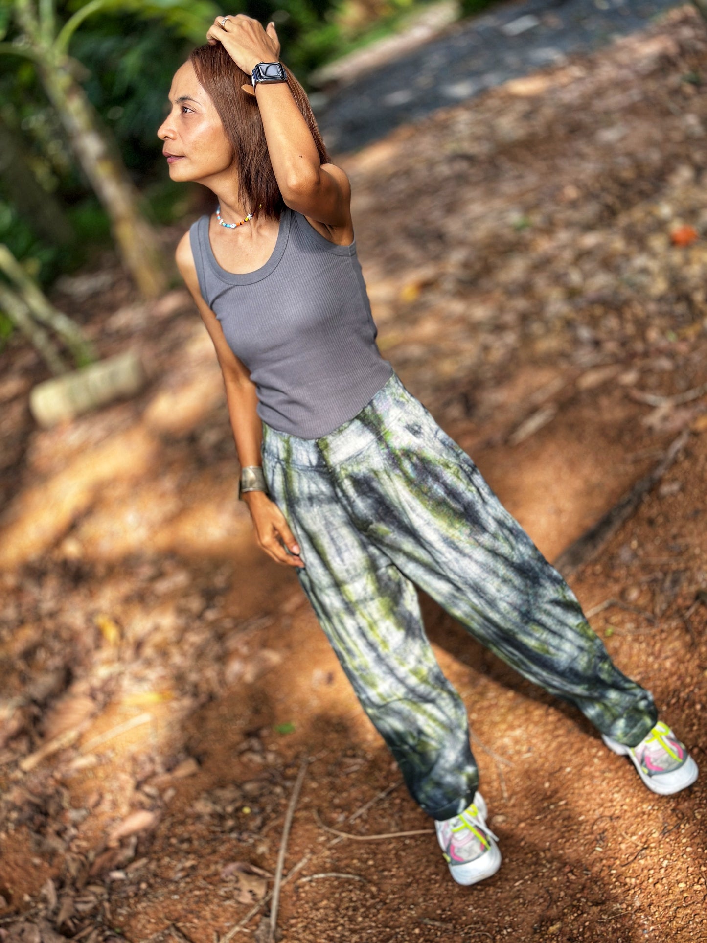 Nuichan tie-dye hemp pants made from sustainable handwoven hemp and vintage Hmong hill tribe fabric, featuring a gray-green tie-dye design. These eco-friendly boho trousers, with an elastic back, are photographed against a natural outdoor setting.