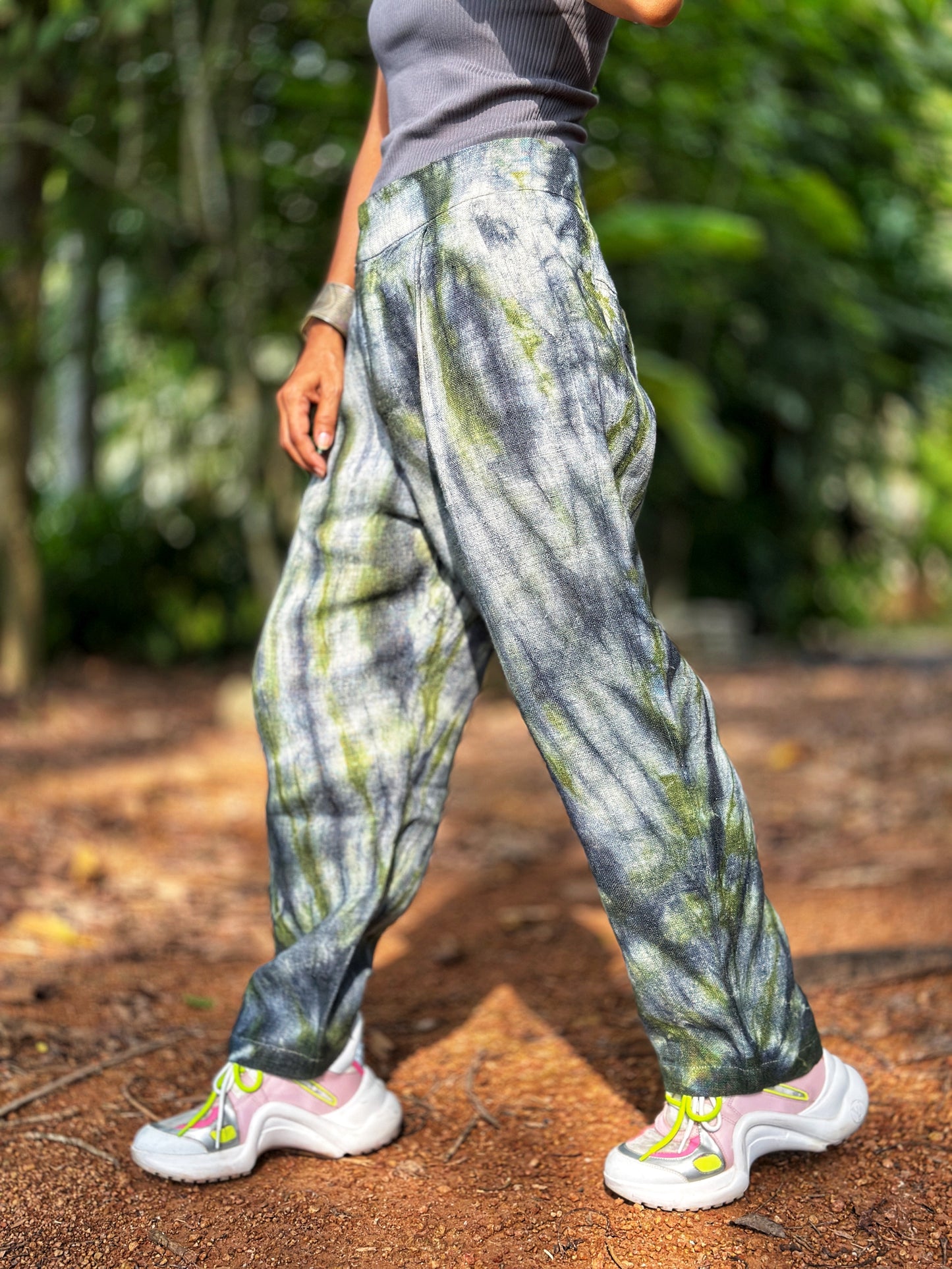 Woman styling Nuichan tie-dye hemp pants in gray-green, paired with a simple top and layered jewelry. These handwoven boho trousers, crafted from Hmong hill tribe fabric.