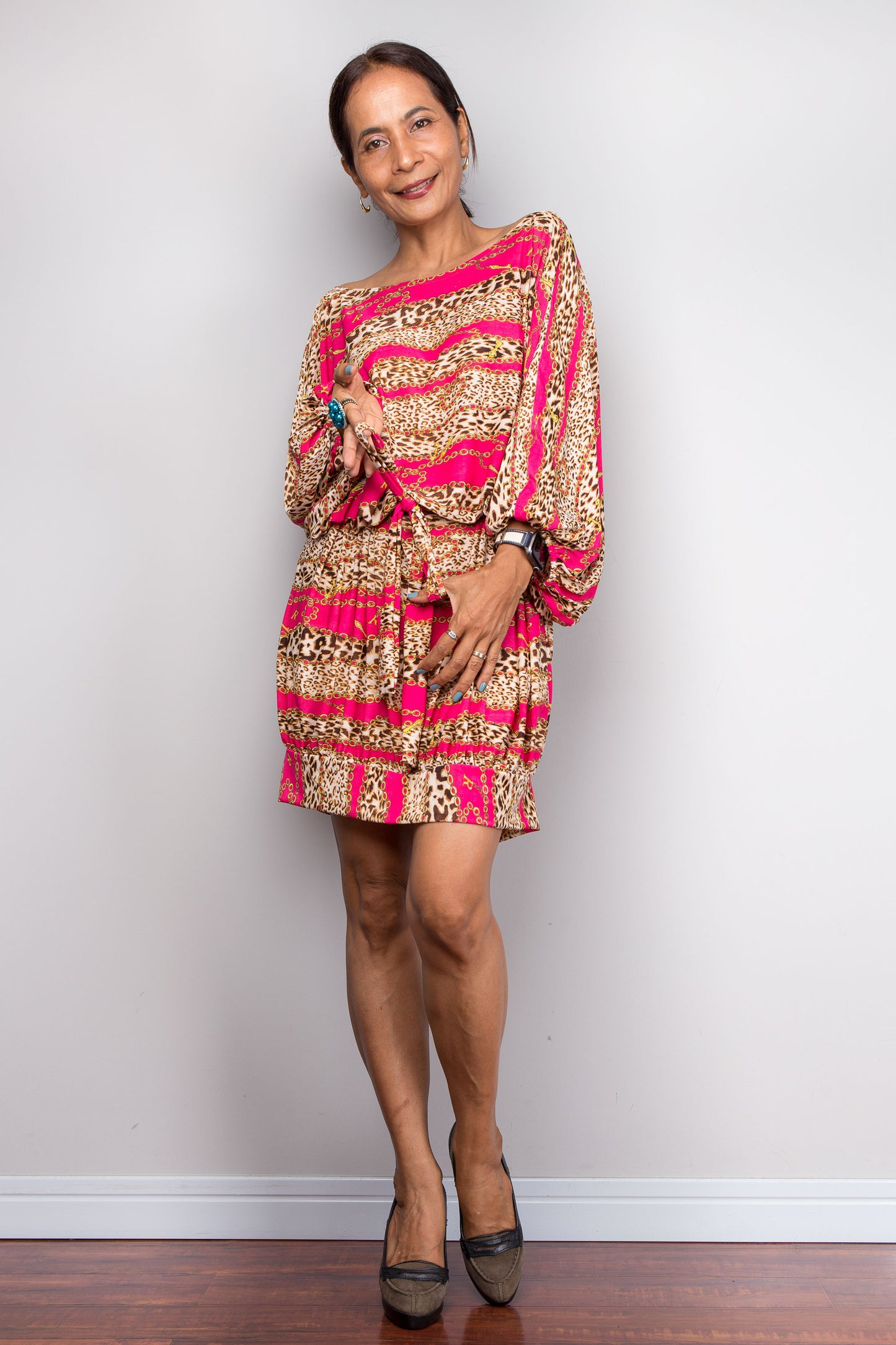 Woman wearing a patterned dress with pink and gold design against a plain background