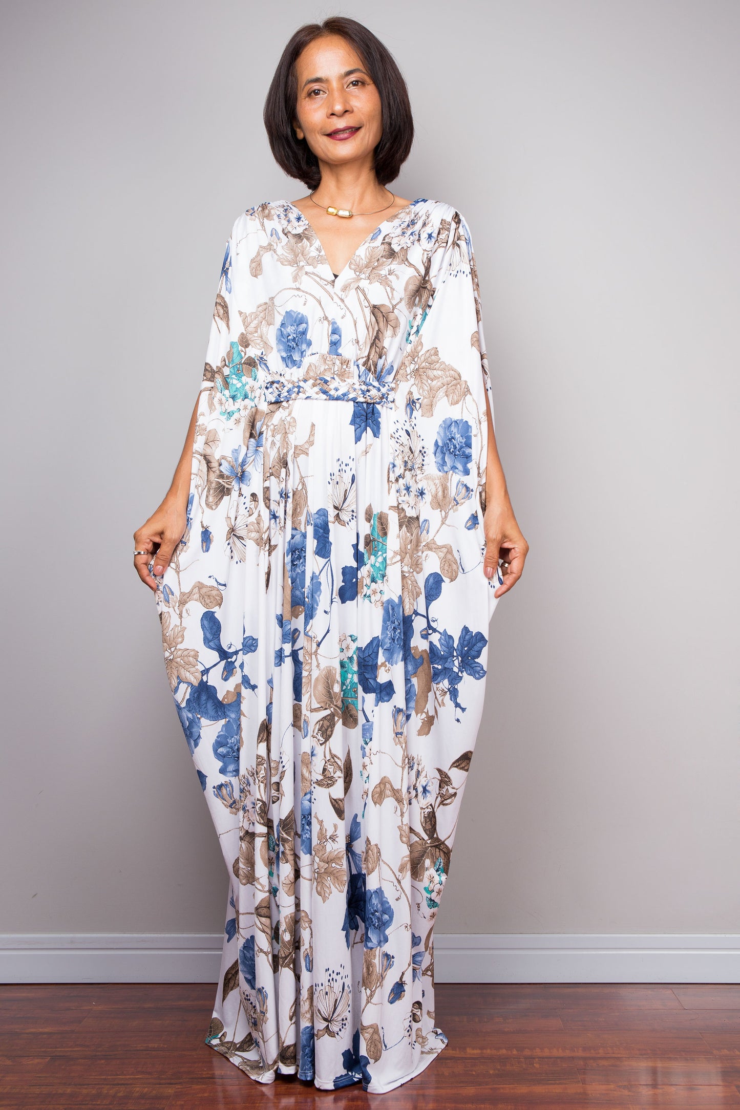 Woman wearing a white floral caftan dress against a plain background
