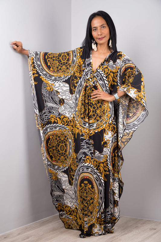 Nuichan’s black and gold baroque kaftan dress with intricate white accents, modeled by a woman with long black hair, posed gracefully in a minimalist studio with a gray background and light wood flooring.