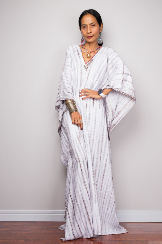 A person wearing an off white tie-dye kaftan dress with wide sleeves and a maxi length.  Nuichan tie dye caftan design