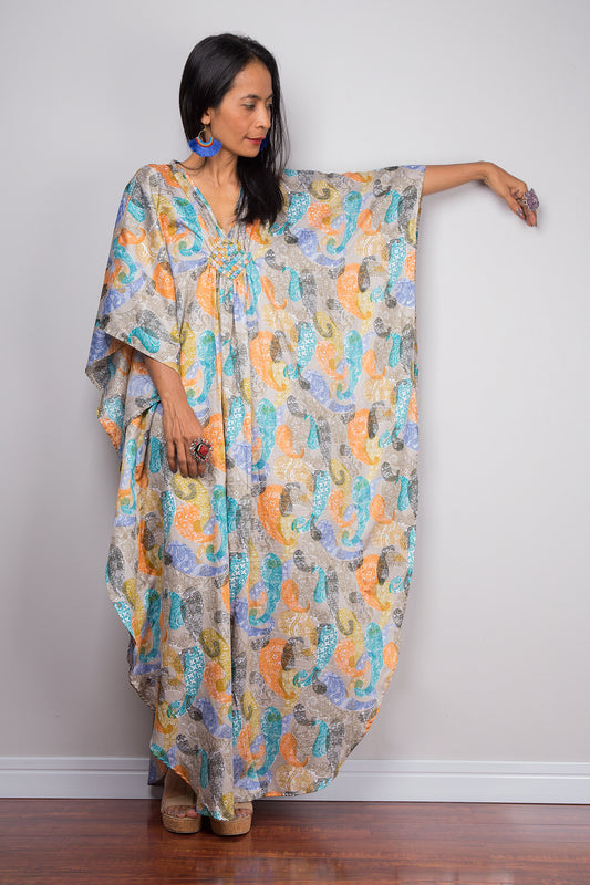 A woman standing and modeling a multicolored paisley kaftan dress with a loose fit and butterfly sleeves.