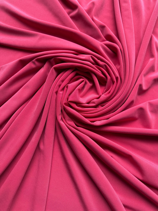 Vibrant pink ITY knit fabric elegantly swirled into a central rosette spiral, showcasing its soft drape, smooth texture, and fluid folds.