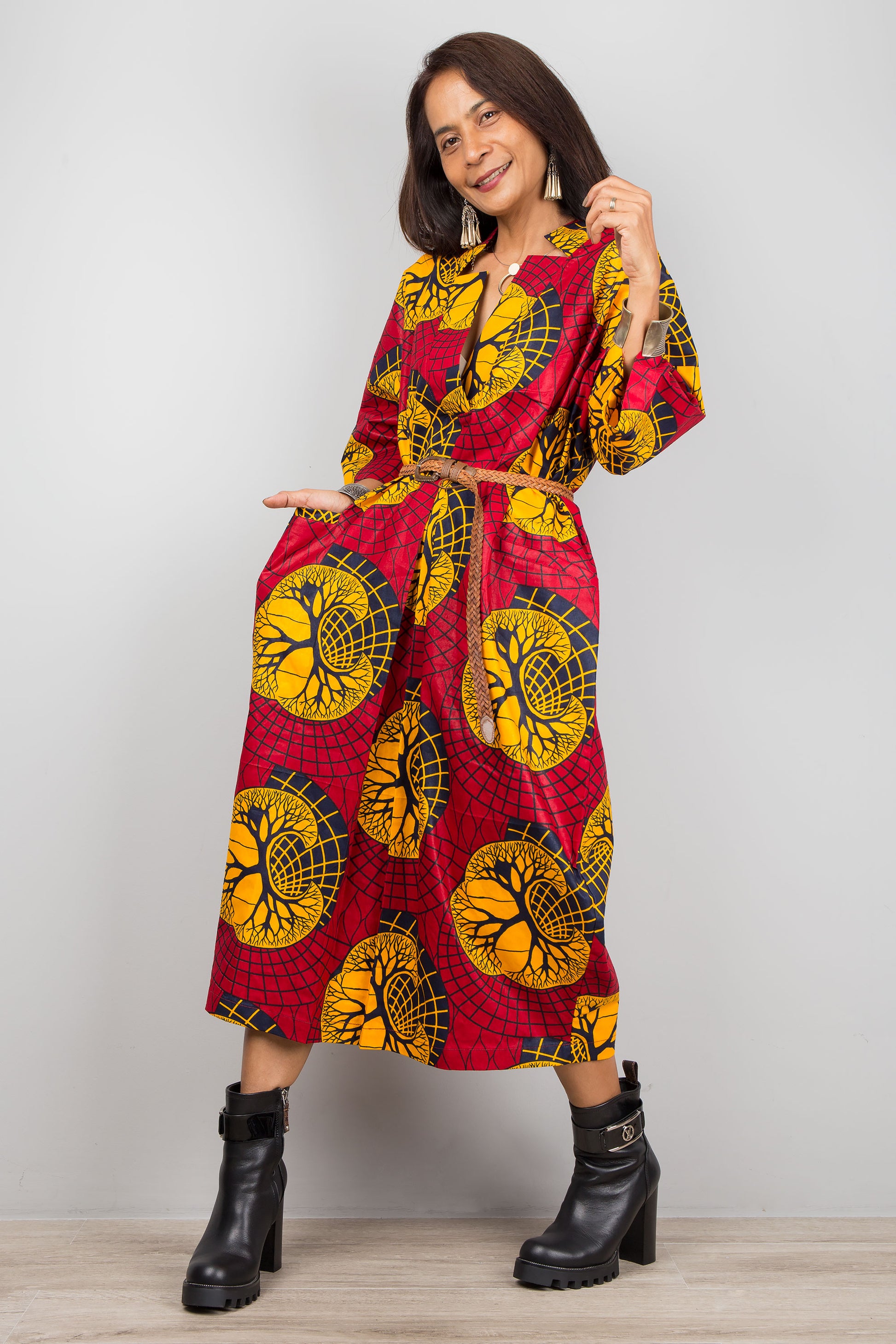 Nuichan red and yellow Ankara kaftan dress with a loose fit, deep V-neckline, and flared sleeves, modeled by a woman against a gray wall and wooden floor, paired with black ankle boots.

