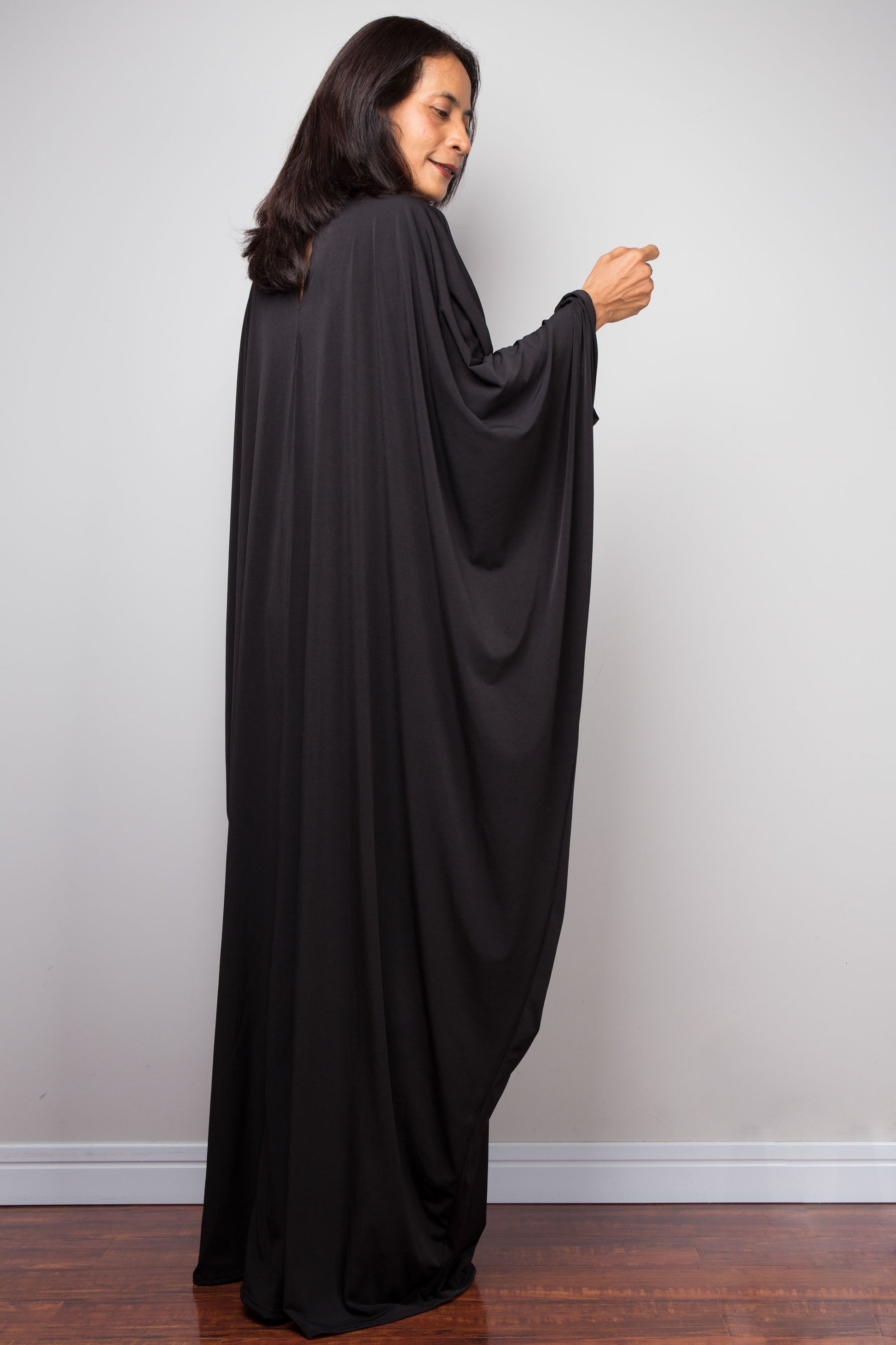 Woman wearing a long black caftan garment against a plain background.  Plus size black dress by Nuichan