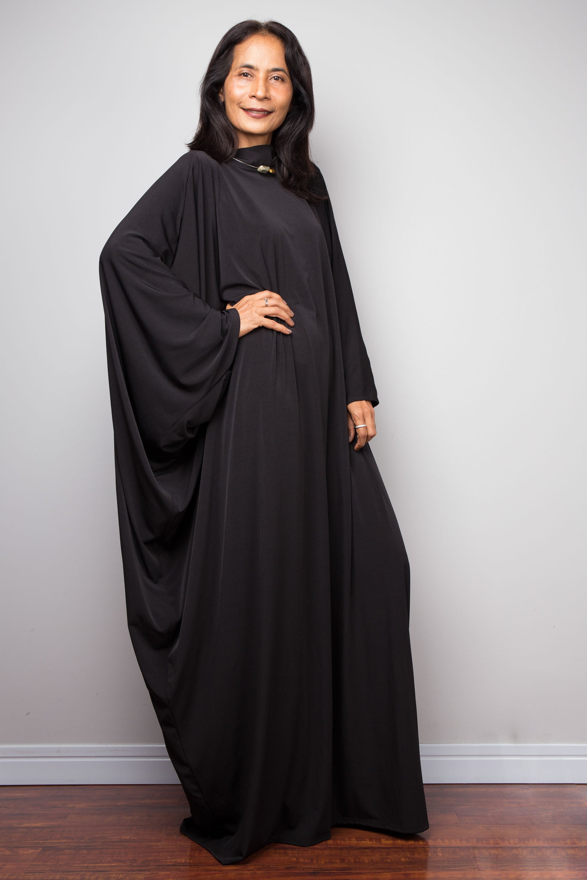 Woman wearing a black dress against a plain background.  Black caftan dress by Nuichan