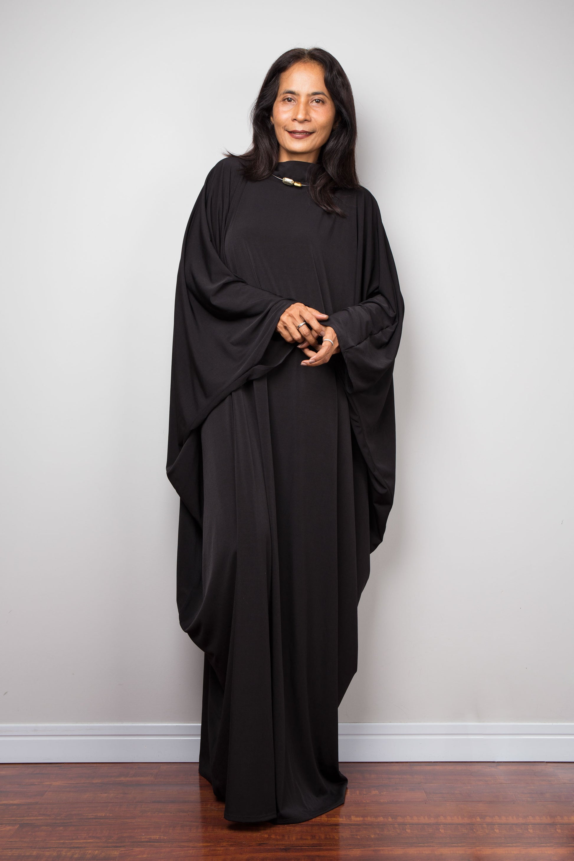 Person wearing a black caftan dress standing against a plain white wall.