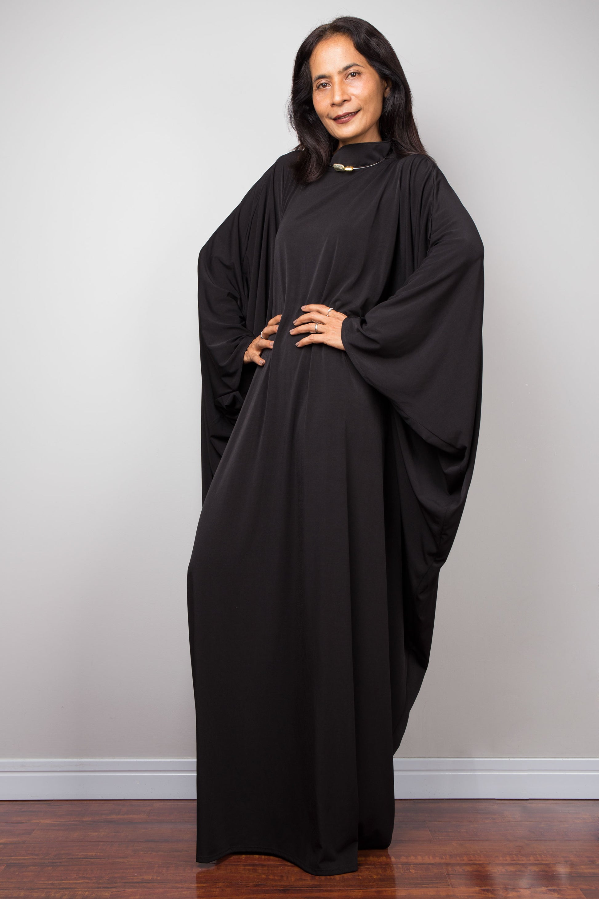 Woman wearing a black abaya dress against a plain background.  Black caftan, plus size dress by Nuichan