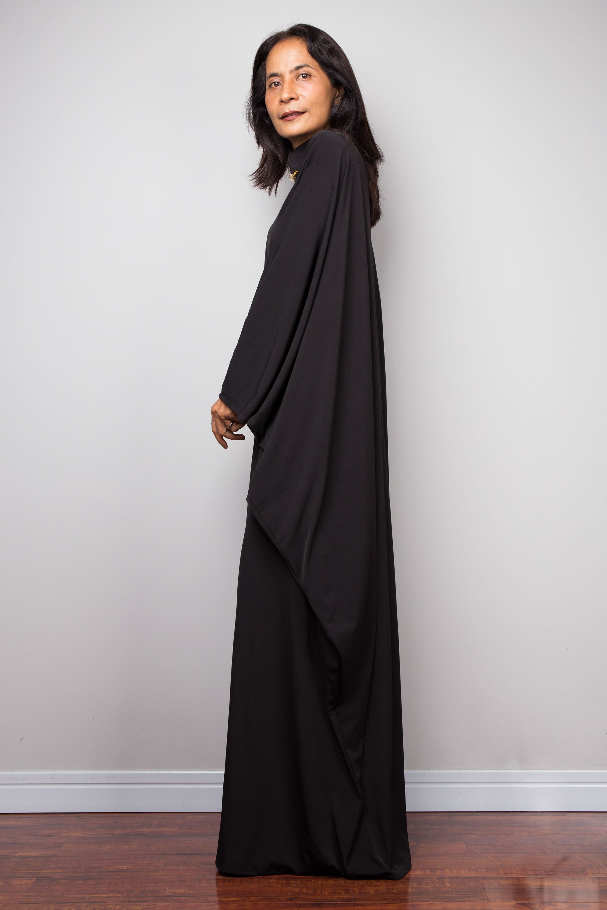 Woman wearing a long black dress against a plain wall.  Black caftan, plus size by Nuichan