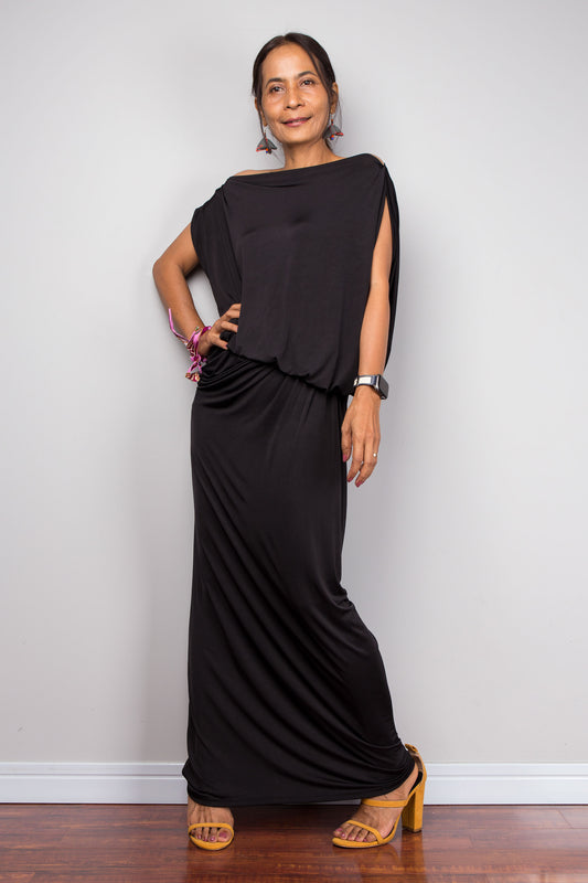 Woman wearing a black sleeveless dress standing against a plain white wall.