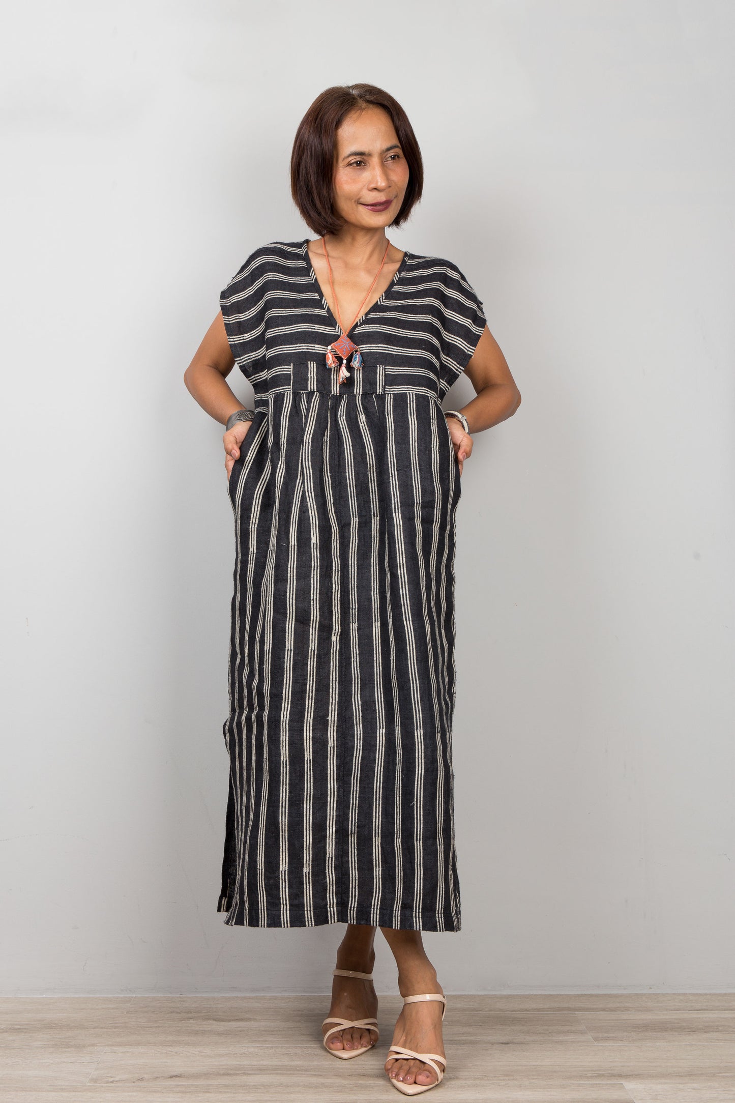 Woman wearing a black caftan with white stripes dress against a plain background