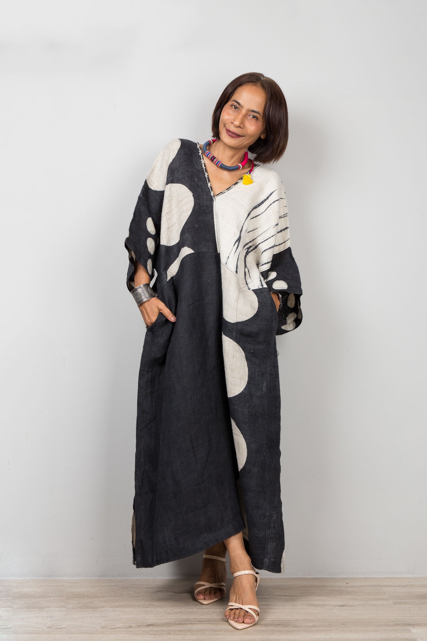 Woman wearing a long, black kaftan with white patterns against a plain background