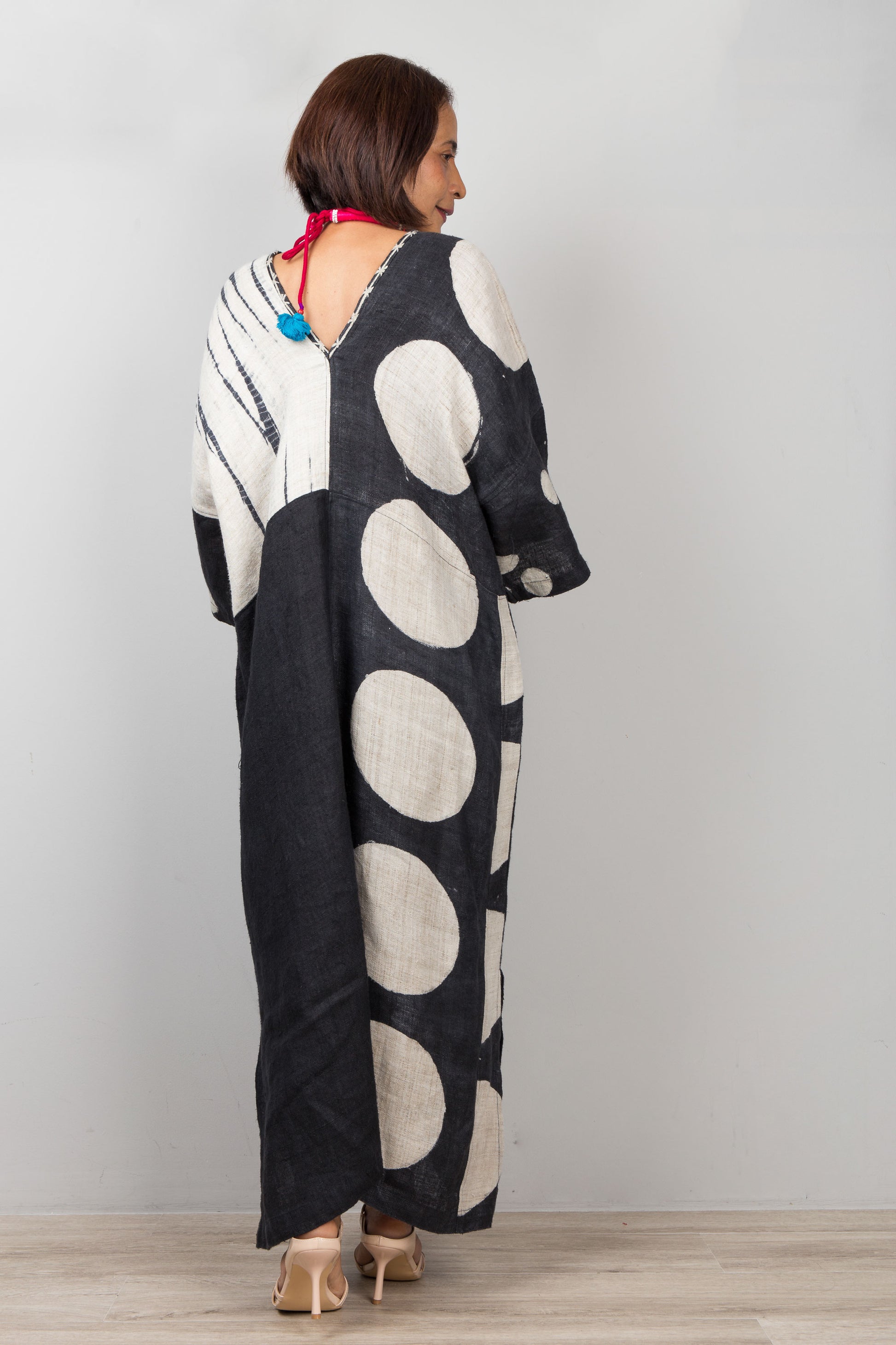 Woman wearing a long, patterned dress with a polka dot design on a plain background