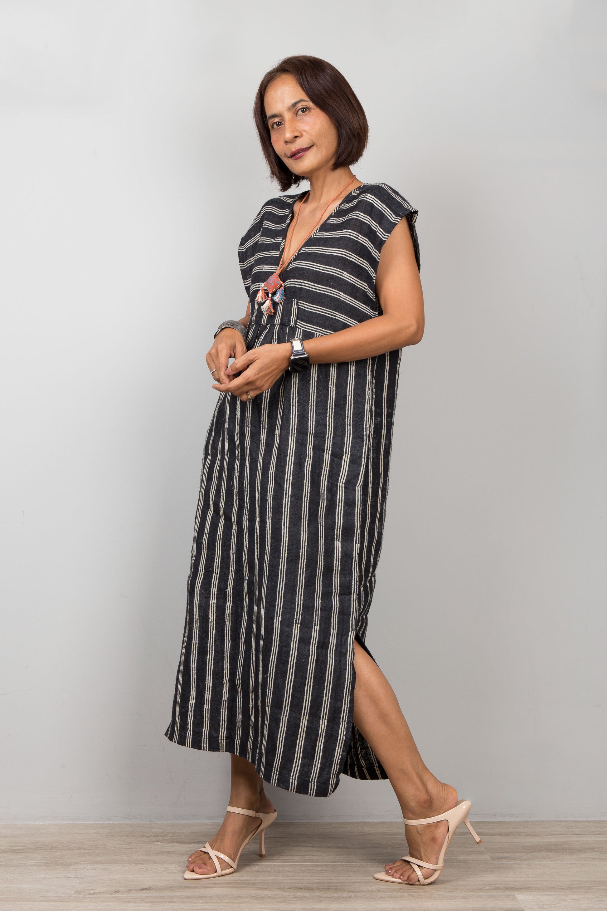 Woman wearing a black kaftan dress with  white stripes against a plain background