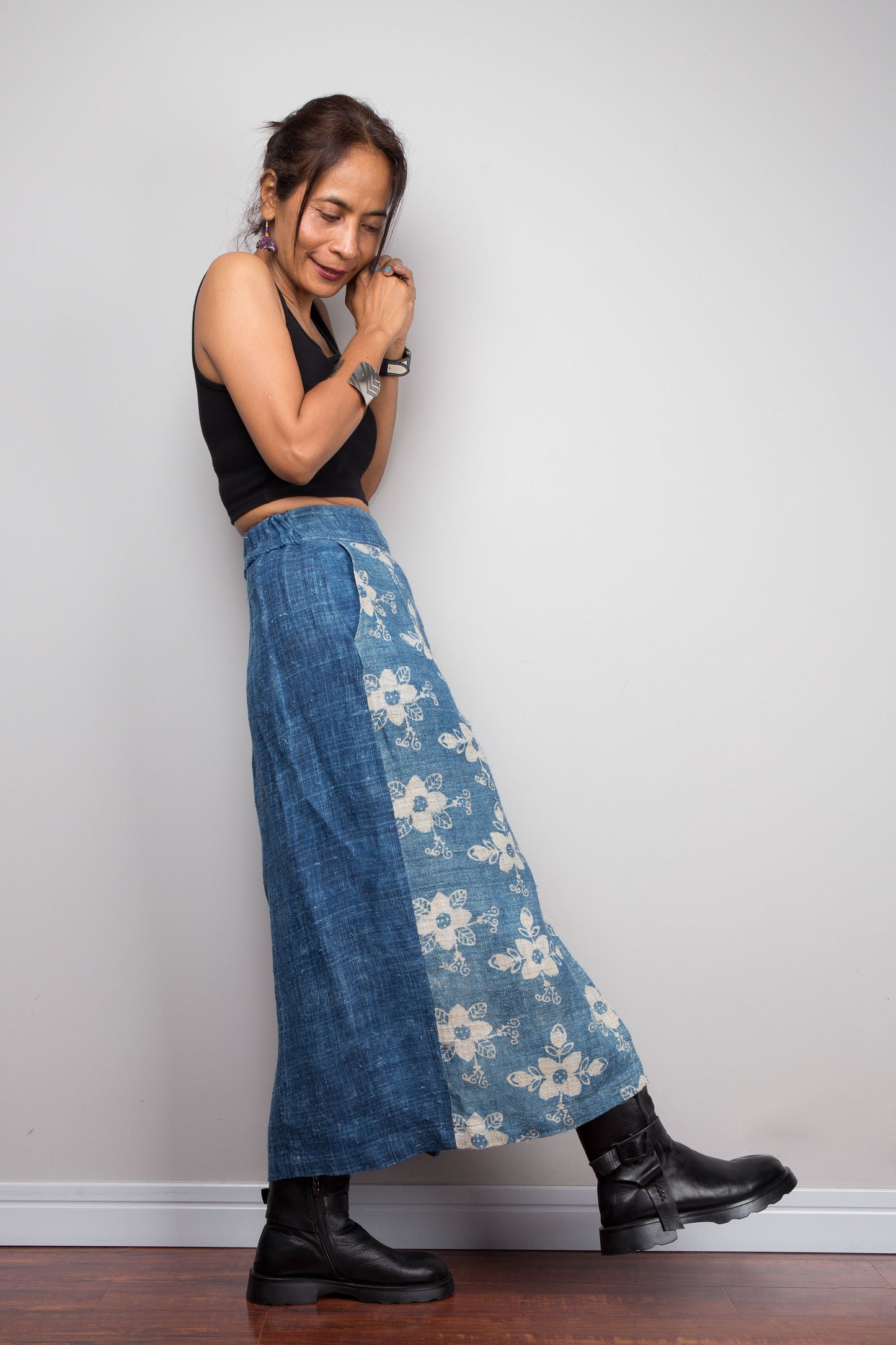 Side view of a model wearing the Nuichan indigo blue handwoven hemp wrap skirt, showcasing the hand block printed floral pattern on the front wrap panel in natural cream on indigo blue, wrap front construction, and elastic waistband, styled with a black crop top and ankle boots