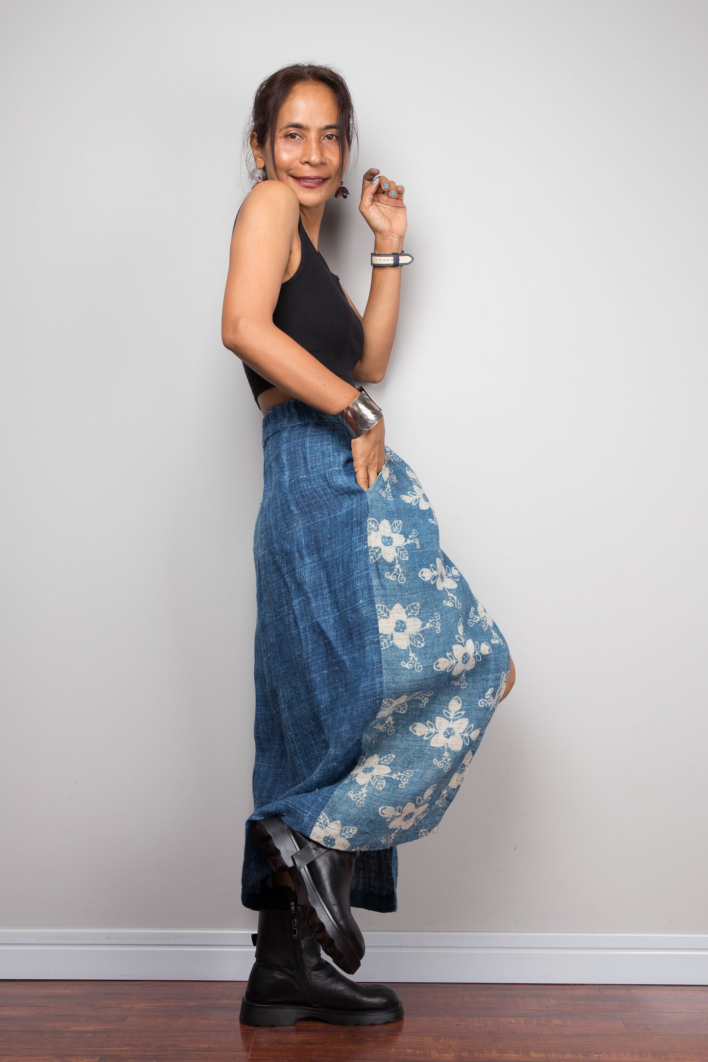 Side view of a model wearing the Nuichan indigo blue handwoven hemp petite wrap, showcasing the hand block printed floral pattern on the front wrap panel in natural cream on indigo blue, wrap front construction with front split opening, and elastic waistband, styled with a black crop top and ankle boots