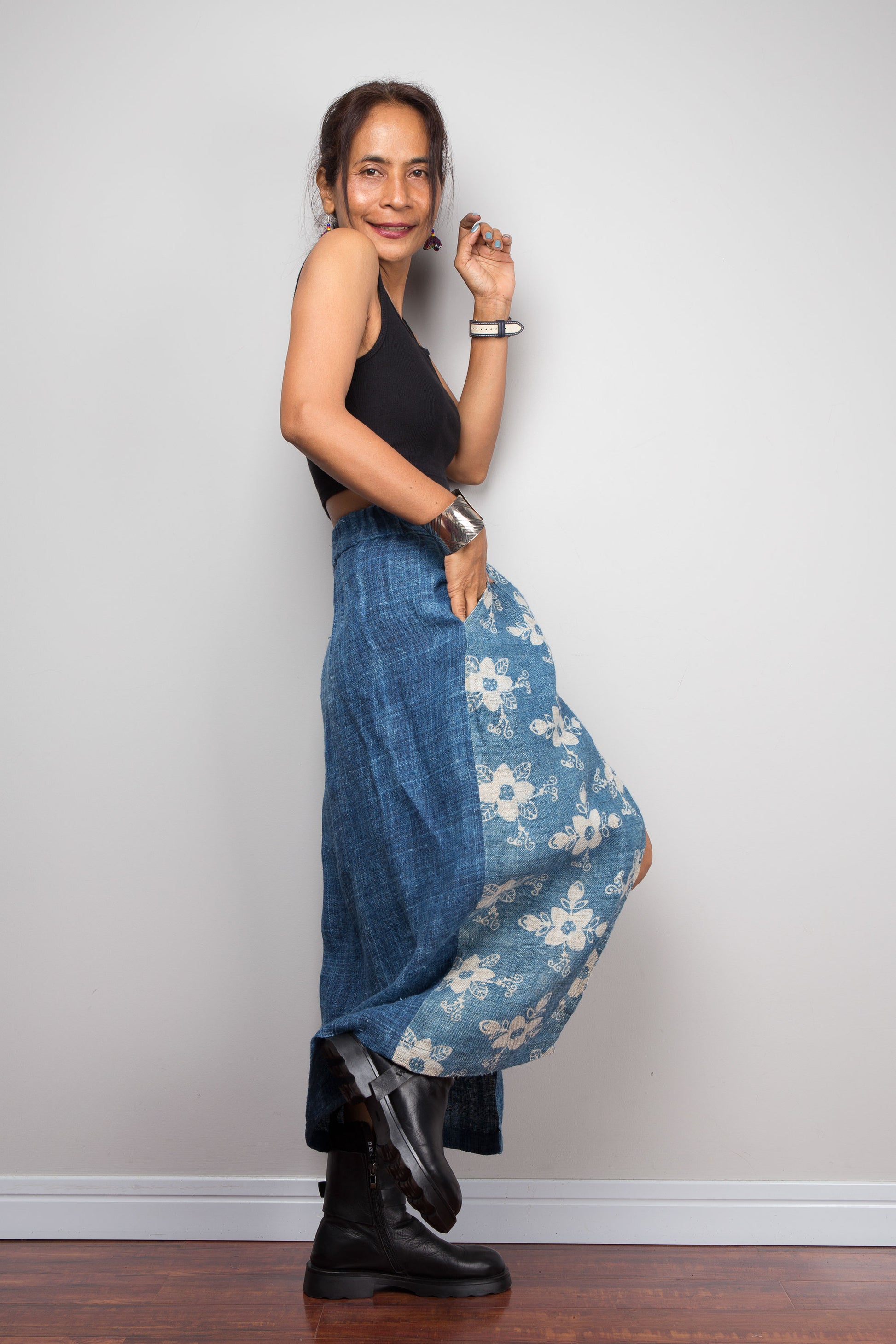 Side view of a model wearing the Nuichan indigo blue handwoven hemp petite wrap, showcasing the hand block printed floral pattern on the front wrap panel in natural cream on indigo blue, wrap front construction with front split opening, and elastic waistband, styled with a black crop top and ankle boots