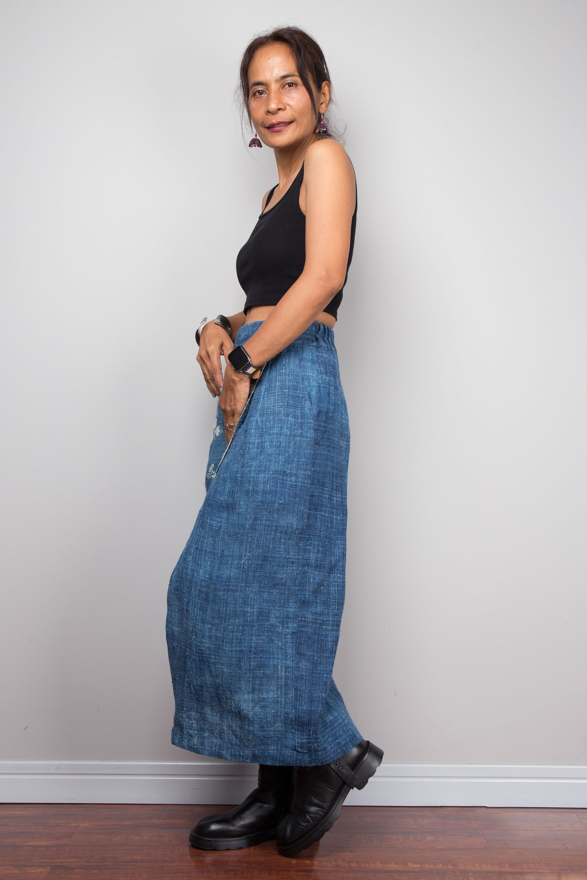 Side view of a model wearing the Nuichan indigo blue handwoven hemp wrap skirt, showcasing the indigo blue, and elastic waistband, styled with a black crop top and ankle boots