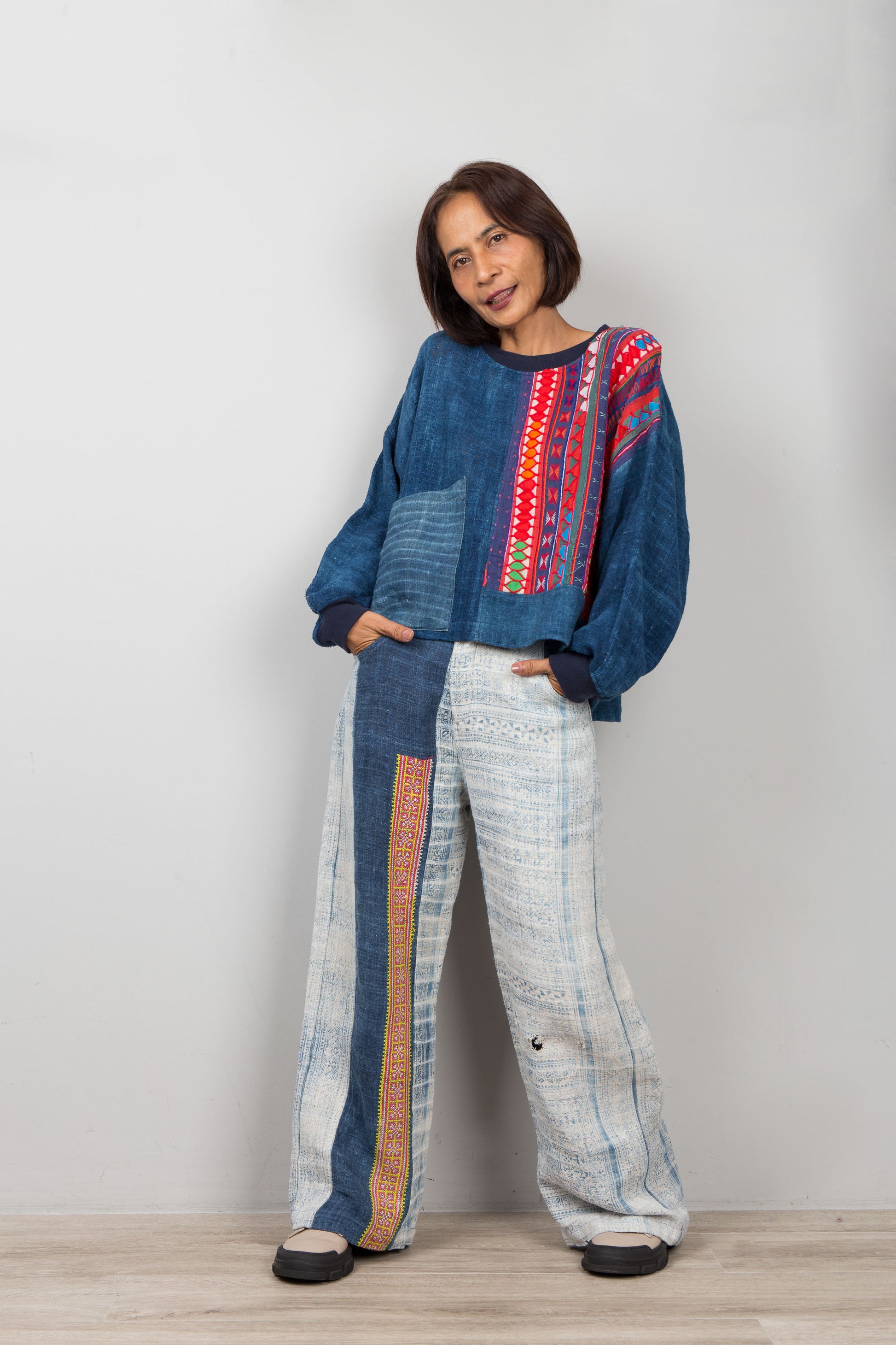 Woman wearing a blue hemp sweater with colorful patterns and light-colored pants against a plain background
