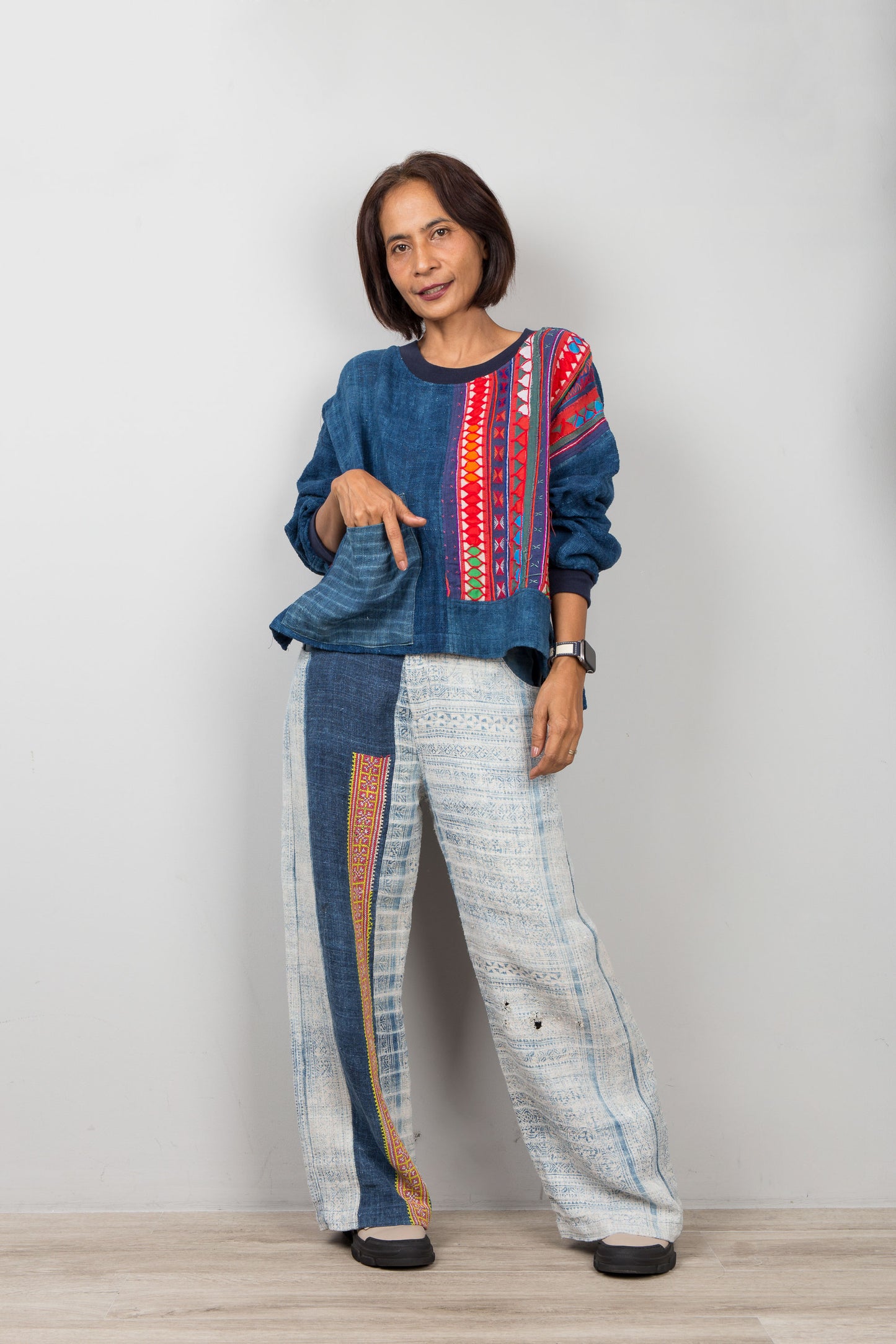 Woman wearing a colorful patchwork hemp sweater and patterned pants on a plain background