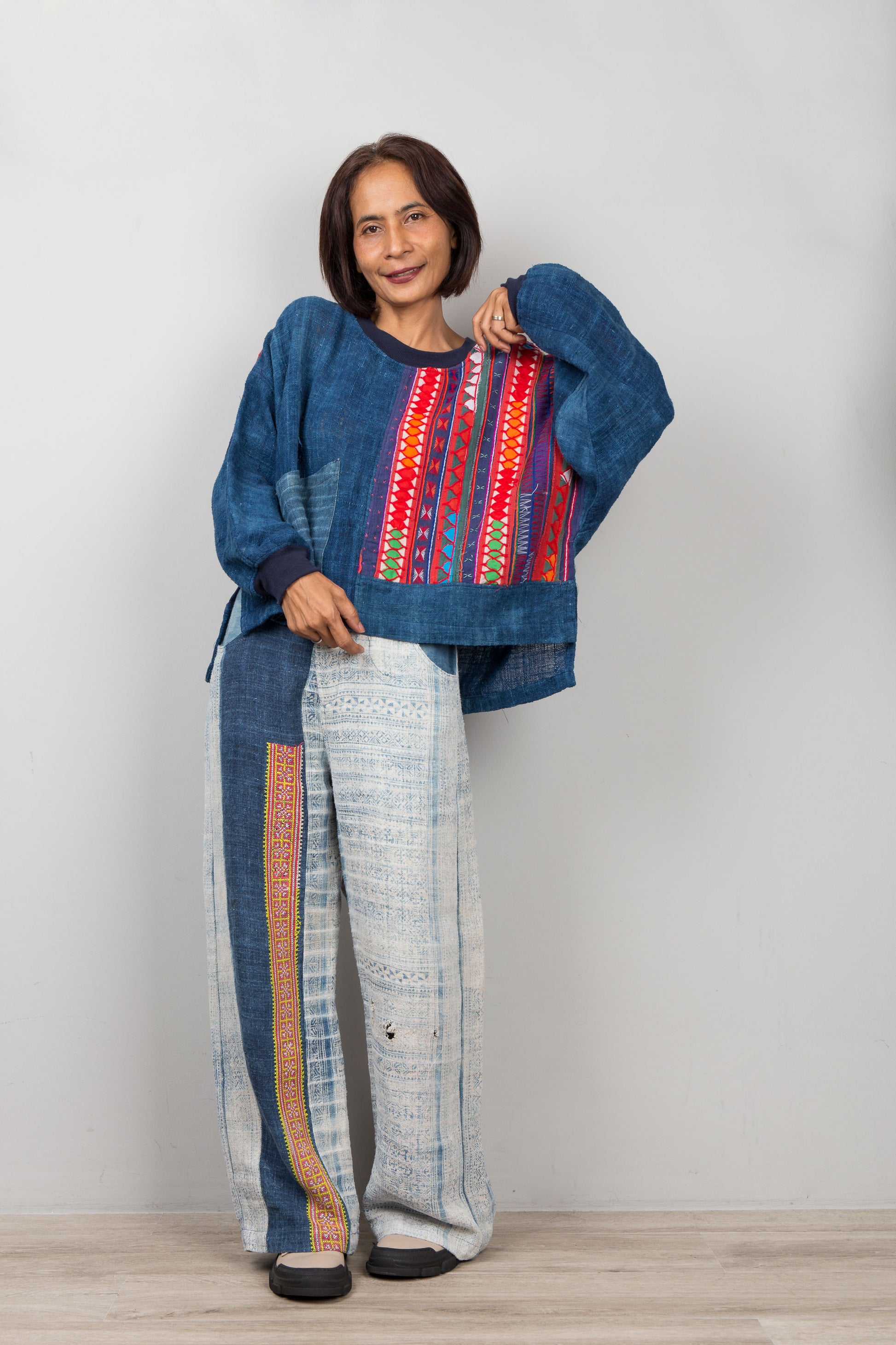 Woman wearing a colorful blue hemp sweater top and patterned pants against a plain background