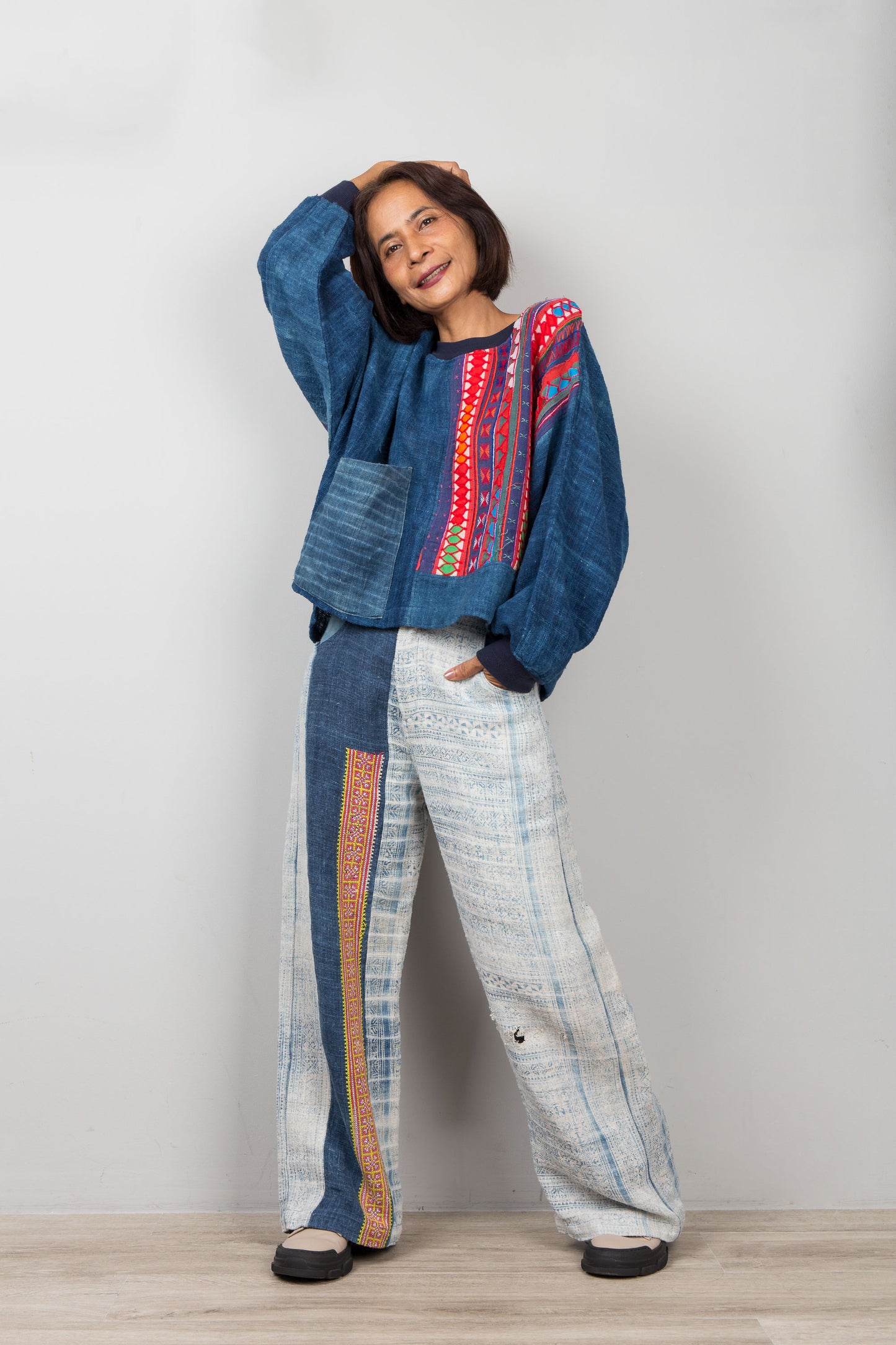 Person wearing a blue patterned hemp sweater and white pants with colorful stripes against a plain background