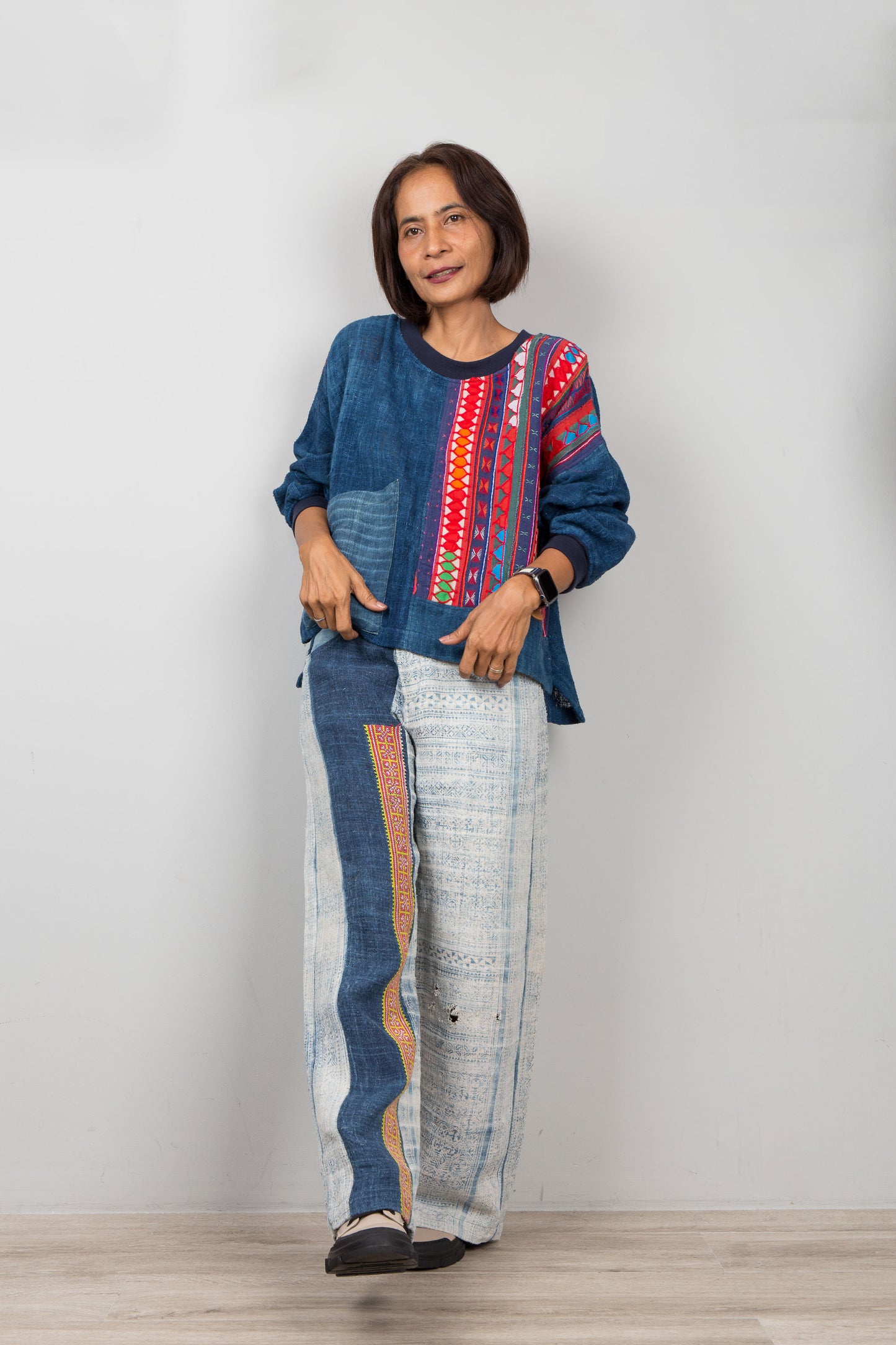 Person wearing a colorful hemp patchwork sweater and patterned pants against a plain background