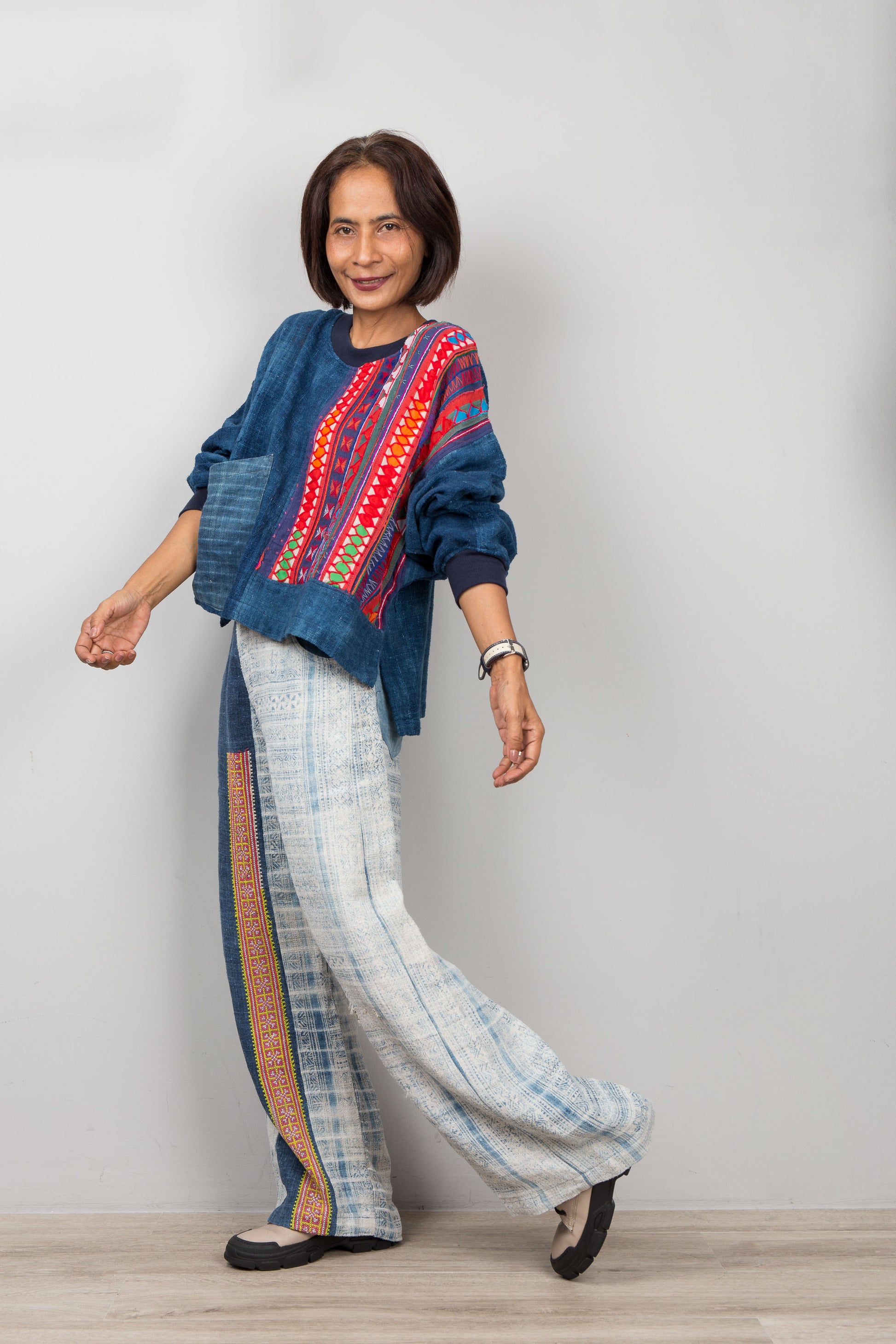 Woman wearing a colorful traditional outfit with a blue hemp top and patterned pants on a plain background