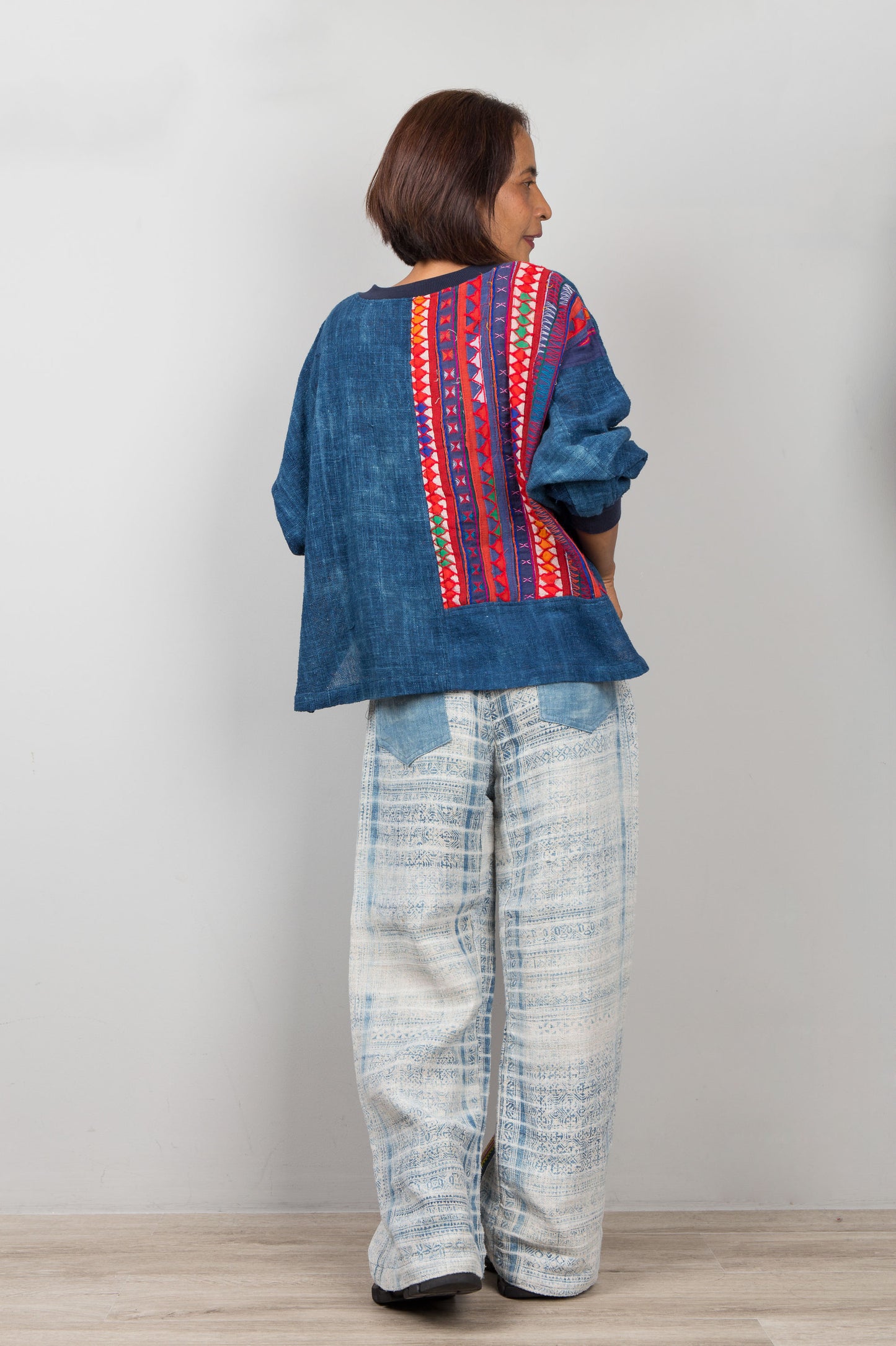 Person wearing a blue sweater top with colorful hemp patterns and light-colored pants on a plain background