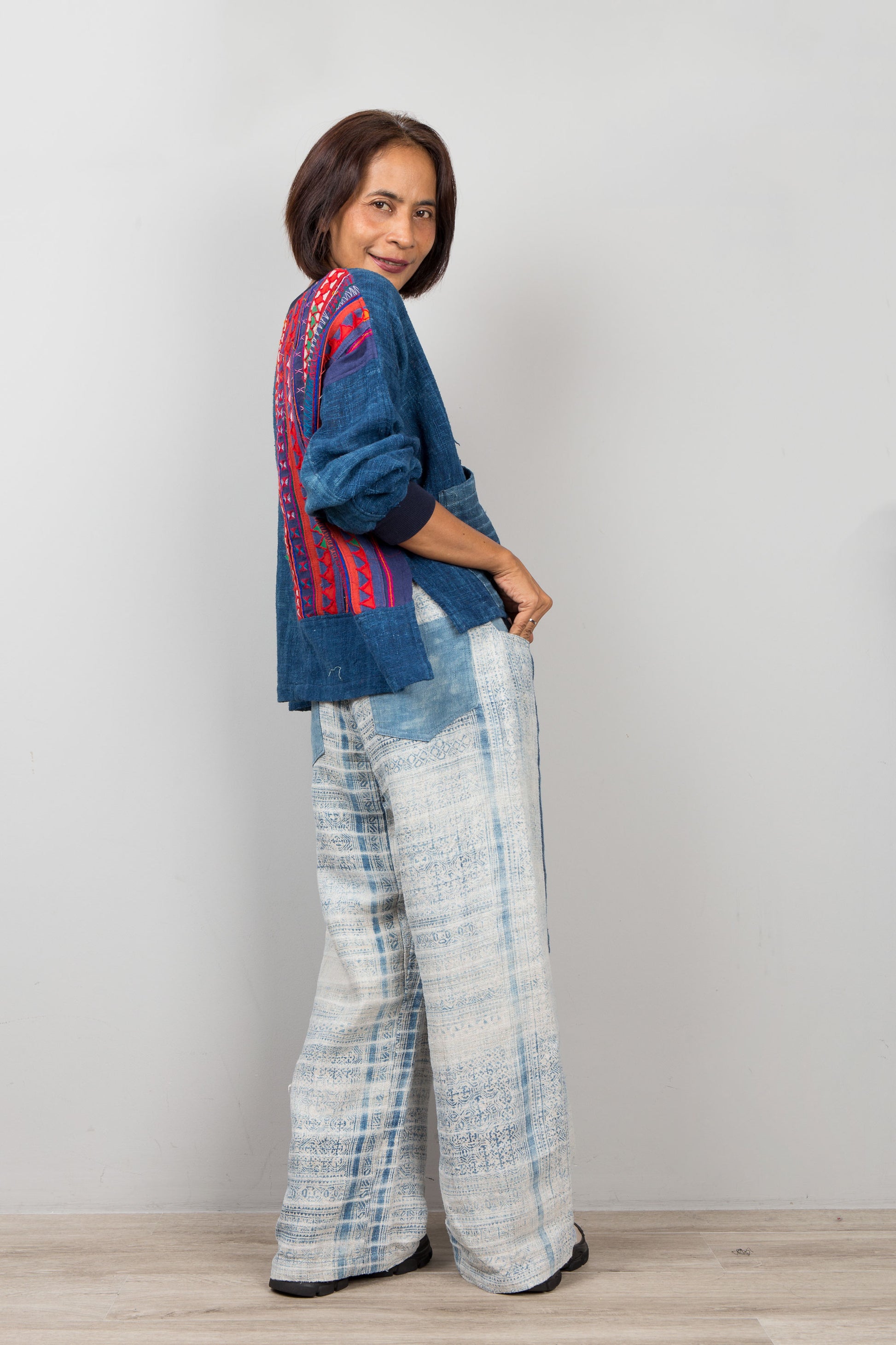Woman wearing a blue embroidered sweater hemp top and plaid pants against a white background