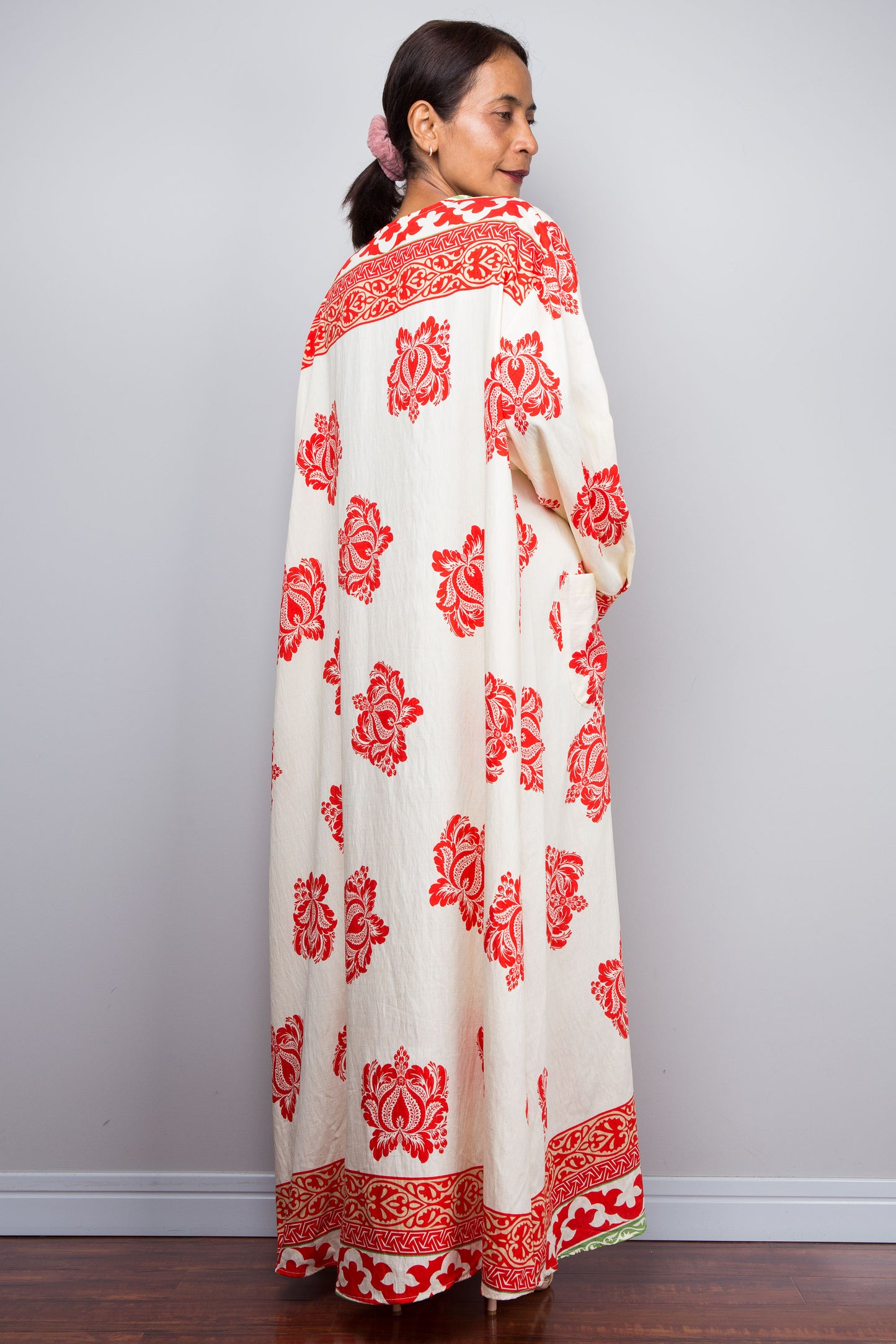 Woman wearing a long, white garment with red floral patterns against a plain background