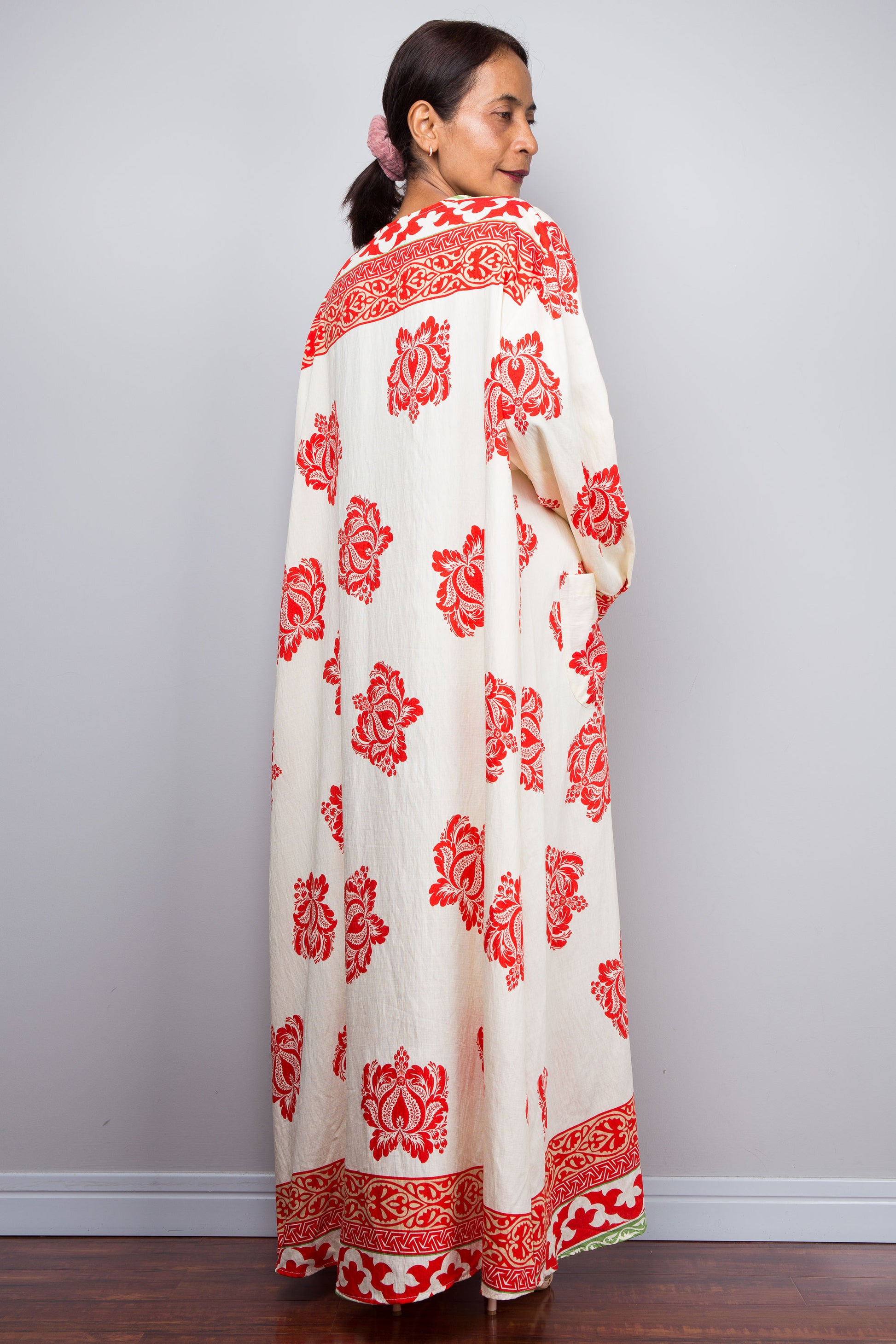 Woman wearing a long, white garment with red floral patterns against a plain background