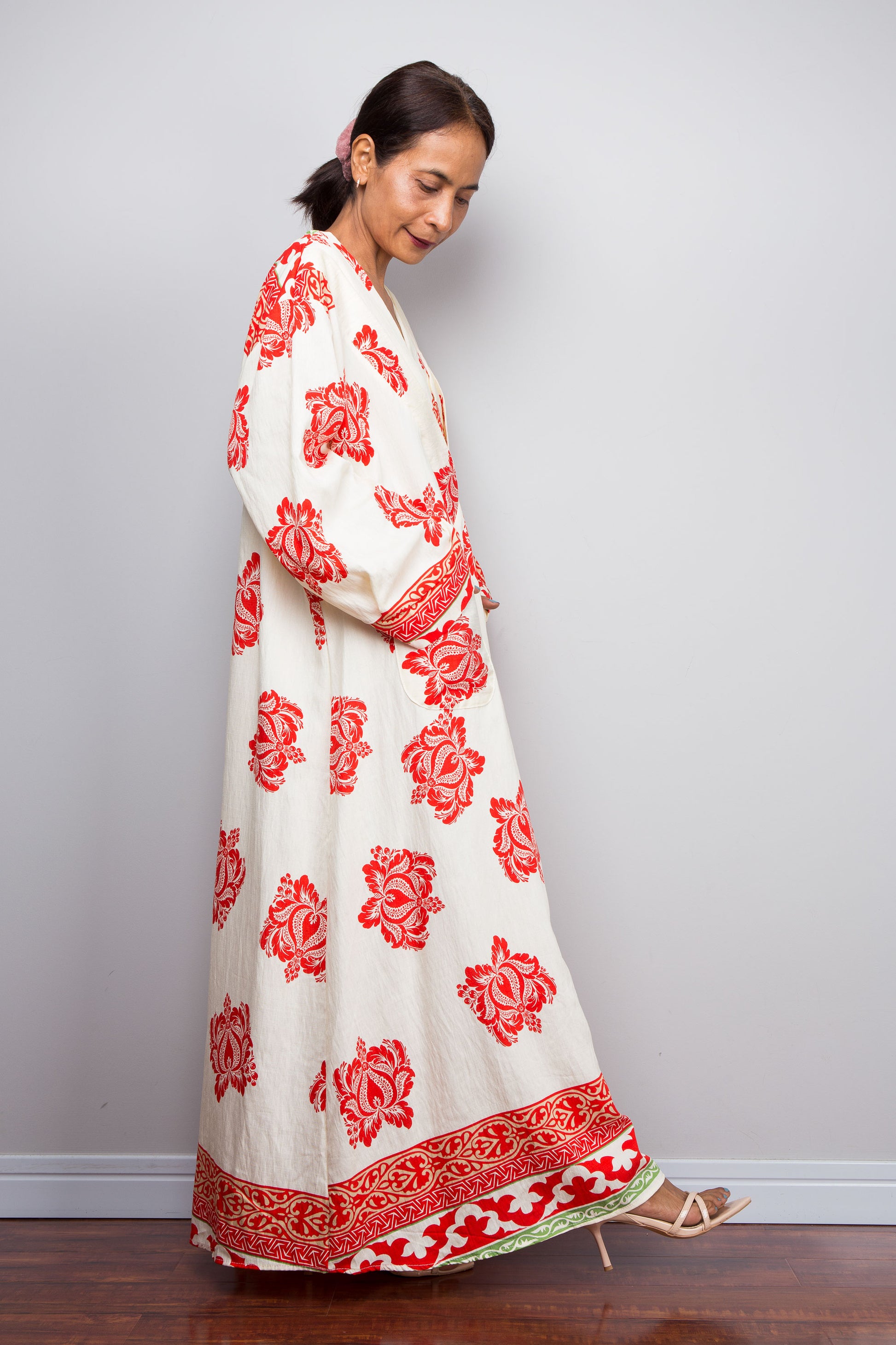 Woman wearing a long, white boho caftan dress with red floral patterns against a plain background