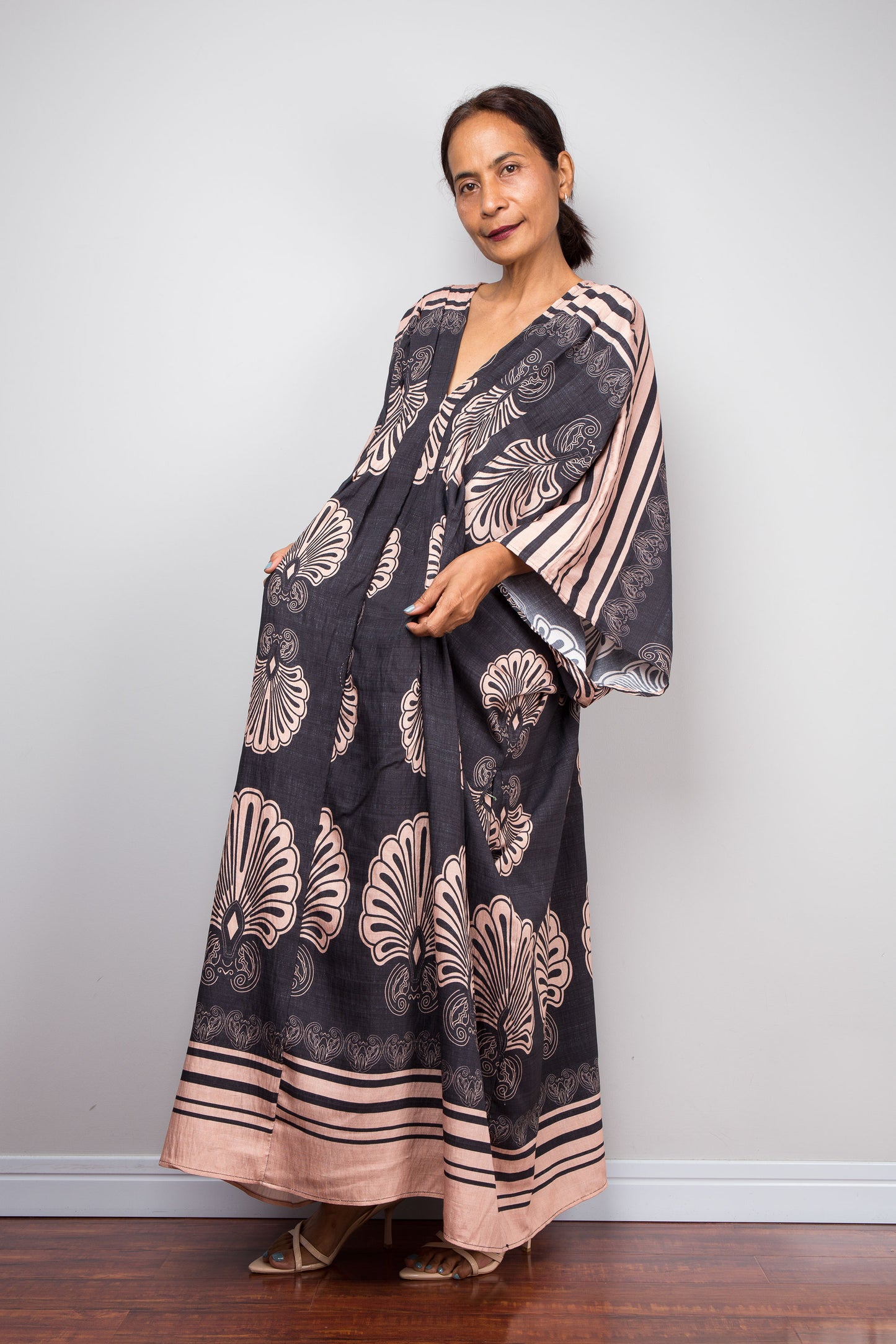 Three quarter shot of a model in the Nuichan charcoal and blush batwing kaftan, displaying the wide kimono sleeves, deep V-neckline, and dramatic shoulder pleating