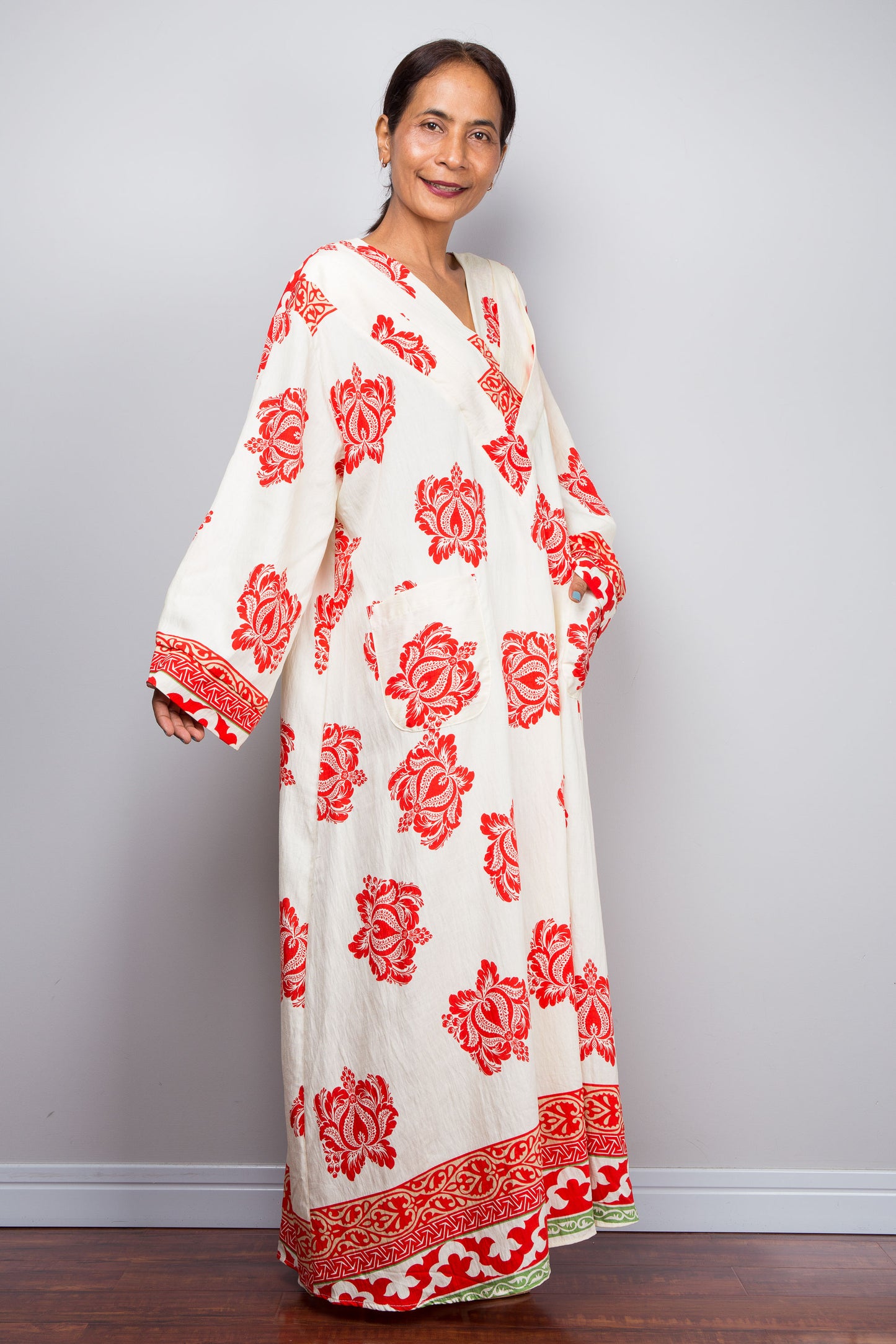 Woman wearing a bohemian caftan dress with red floral patterns against a plain background