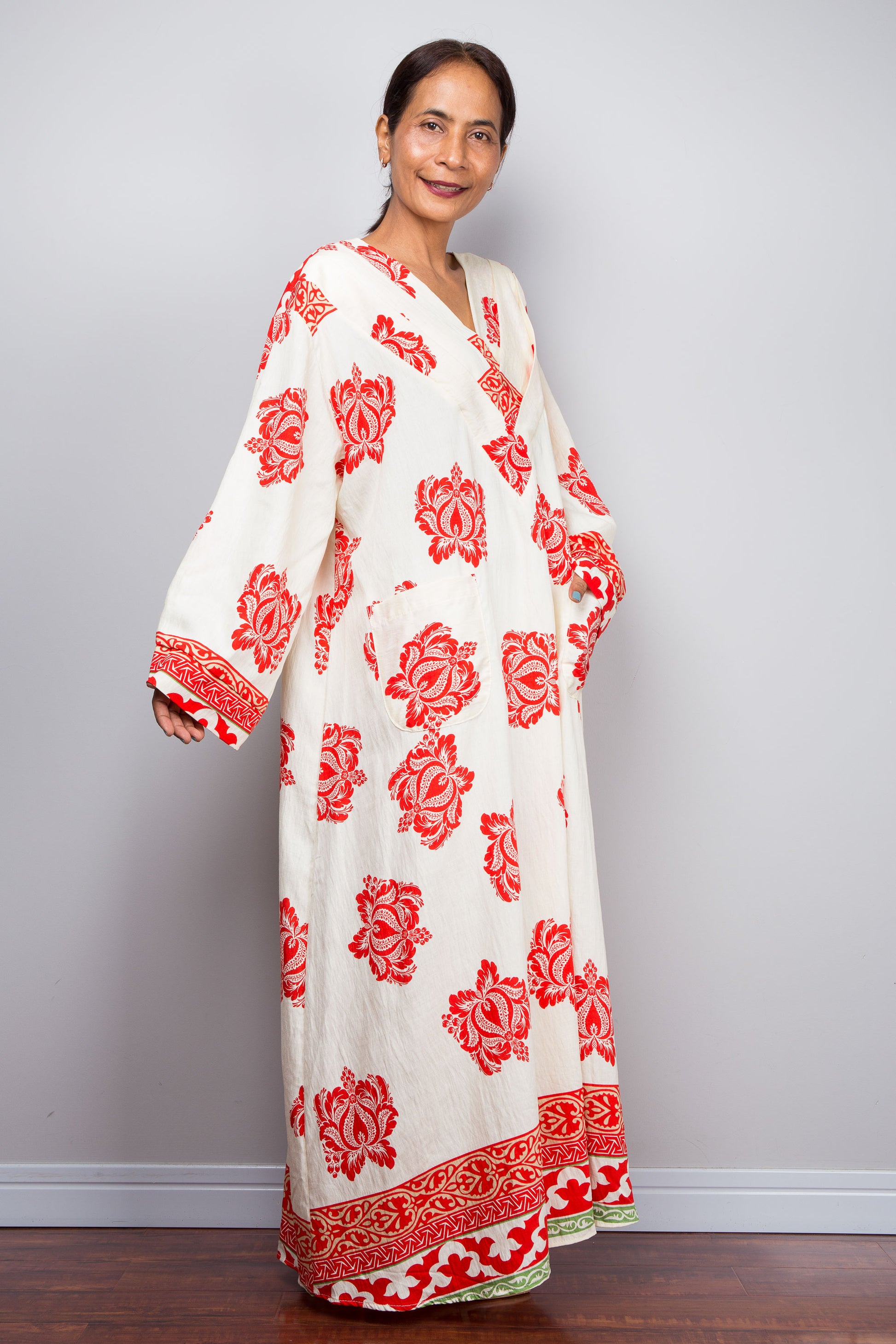 Woman wearing a bohemian caftan dress with red floral patterns against a plain background