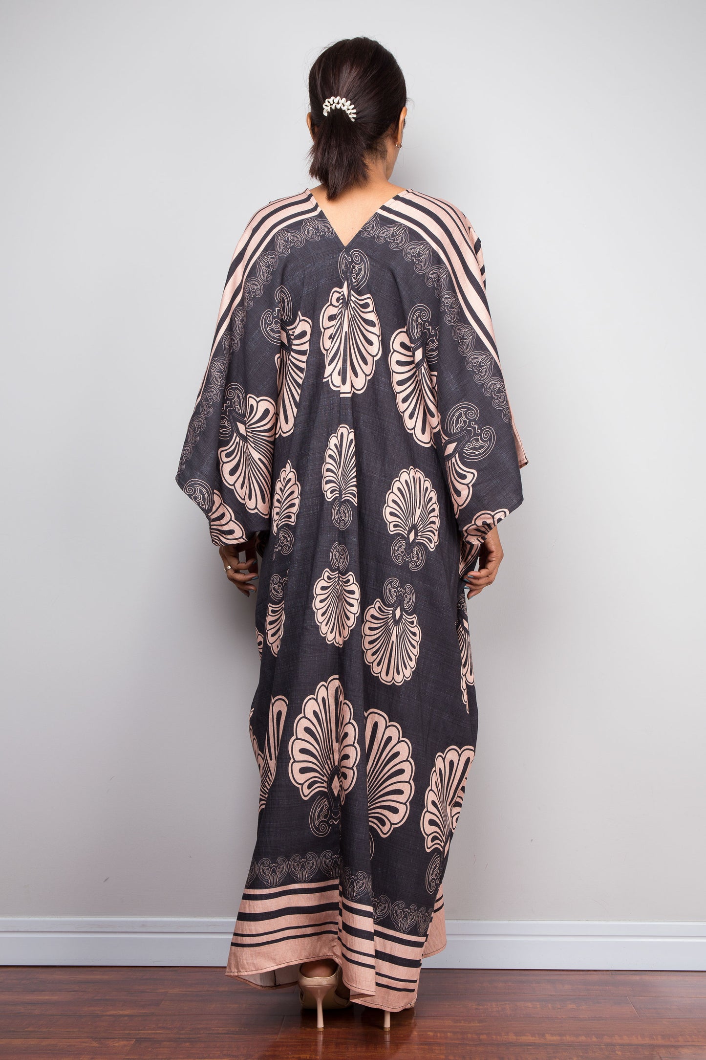 Rear view of a model wearing the Nuichan charcoal grey batwing kaftan dress, highlighting the structural shoulder-to-hem pleating, V-back neckline, and full-length Art Deco fan print sweeping to the floor