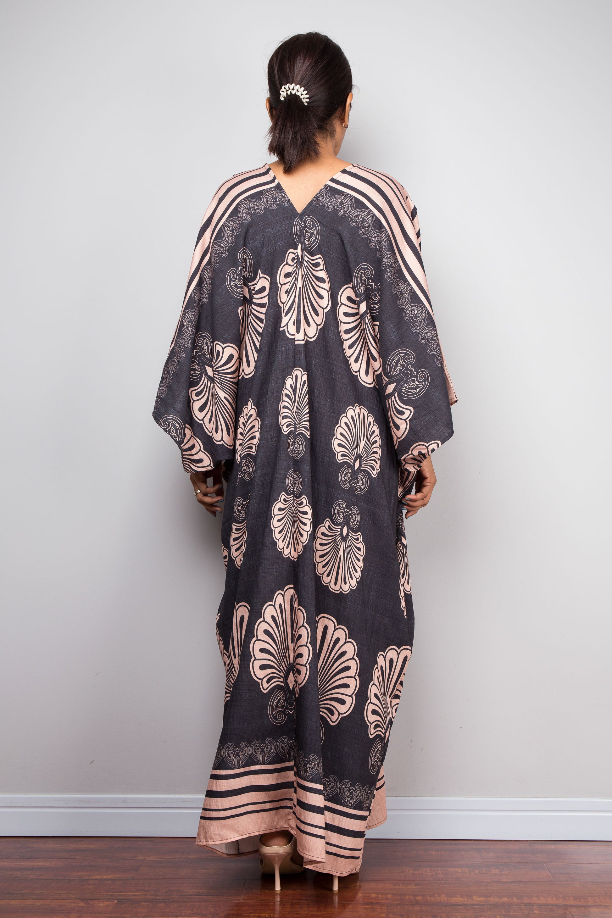 Rear view of a model wearing the Nuichan charcoal grey batwing kaftan dress, highlighting the structural shoulder-to-hem pleating, V-back neckline, and full-length Art Deco fan print sweeping to the floor