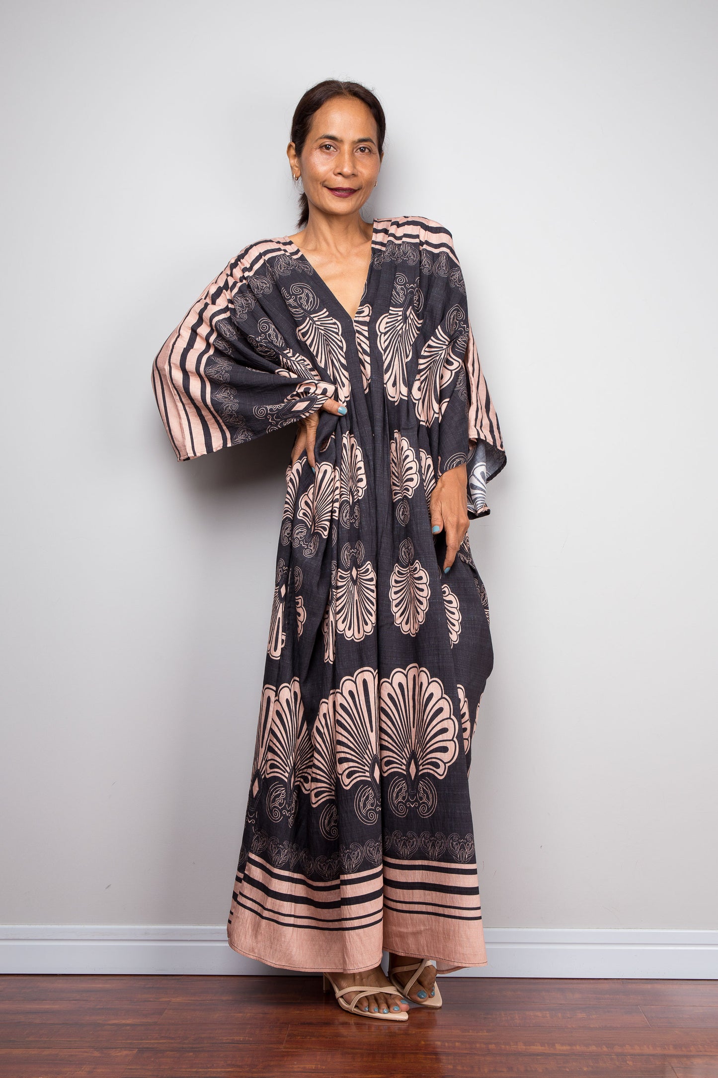 Front-facing shot of a model in the Nuichan charcoal and blush batwing kaftan dress with hand on hip, displaying the wide kimono sleeves with contrasting underside print, deep V-neckline, and dramatic shoulder pleating