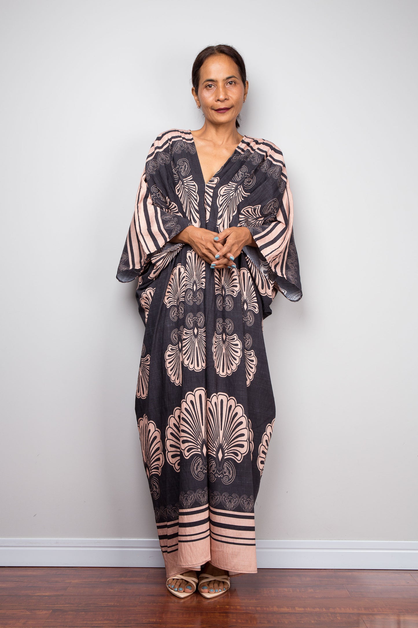 Front-facing studio shot of a model in the Nuichan charcoal and blush batwing kaftan dress with hands crossed over waist, deep V-neckline, and dramatic shoulder pleating