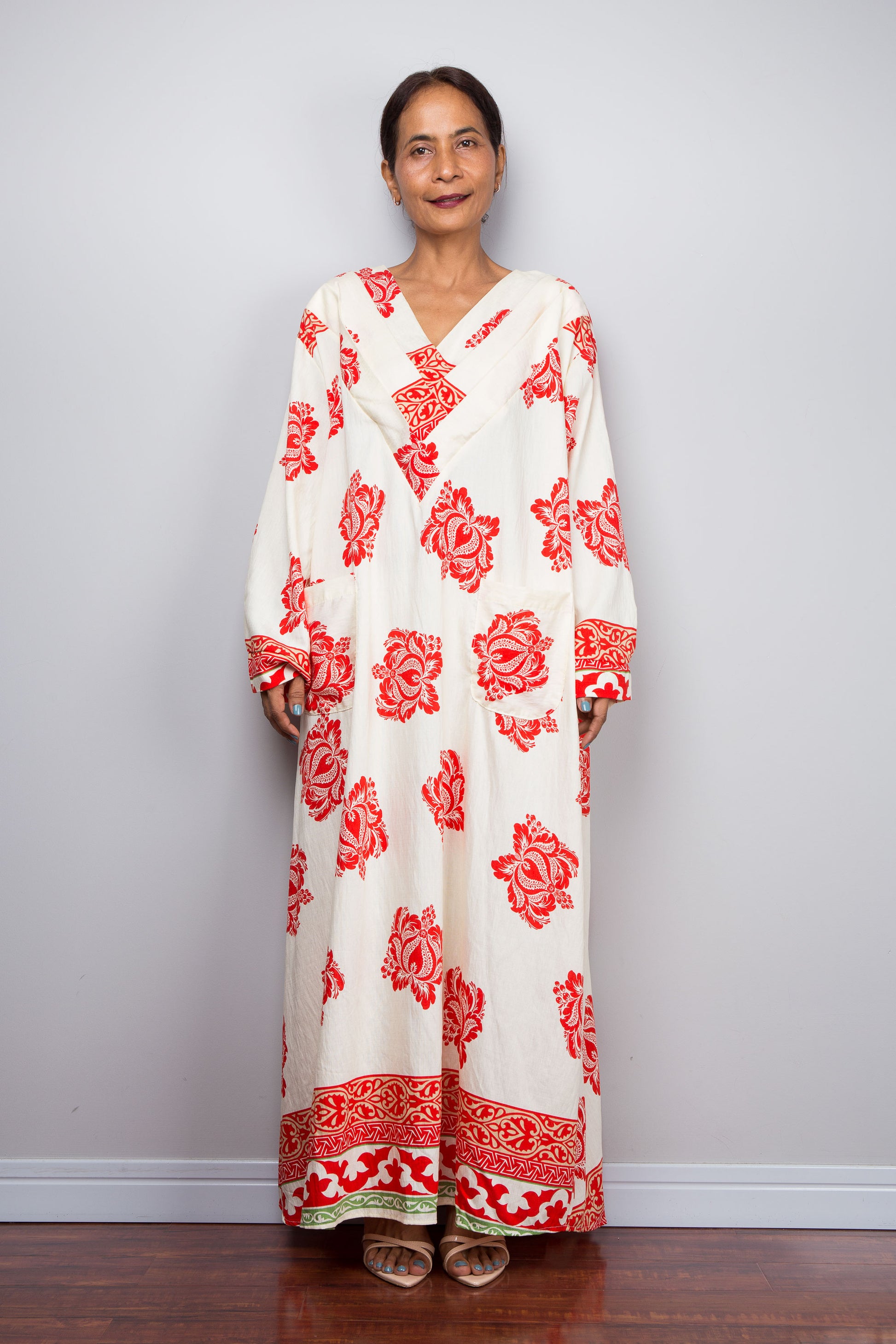 Woman wearing a long, white dress with red floral patterns against a plain background