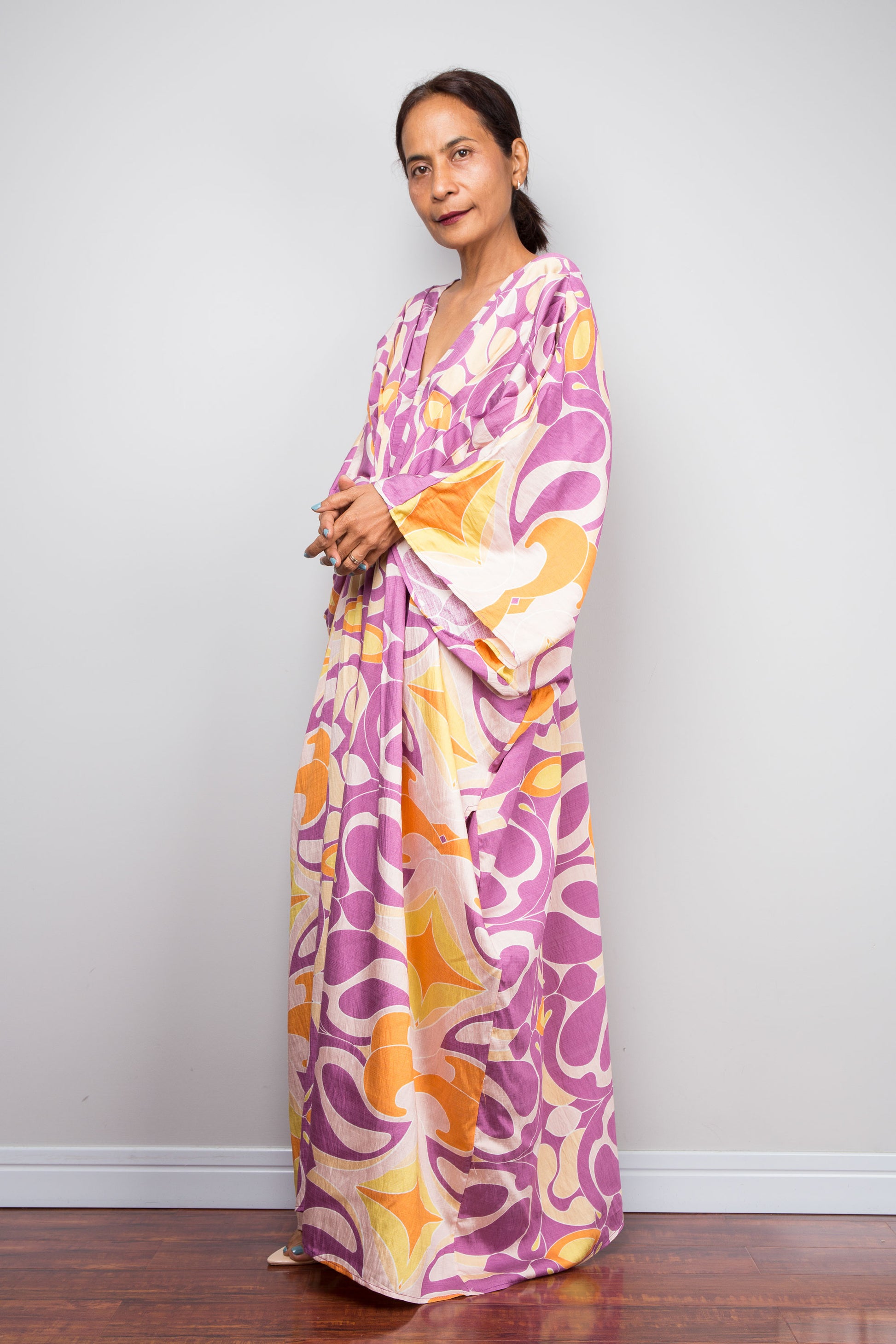 Three quarter studio shot of a model in the Nuichan violet and amber batwing kaftan dress, displaying the wide kimono sleeves, deep V neckline, and dramatic shoulder pleating