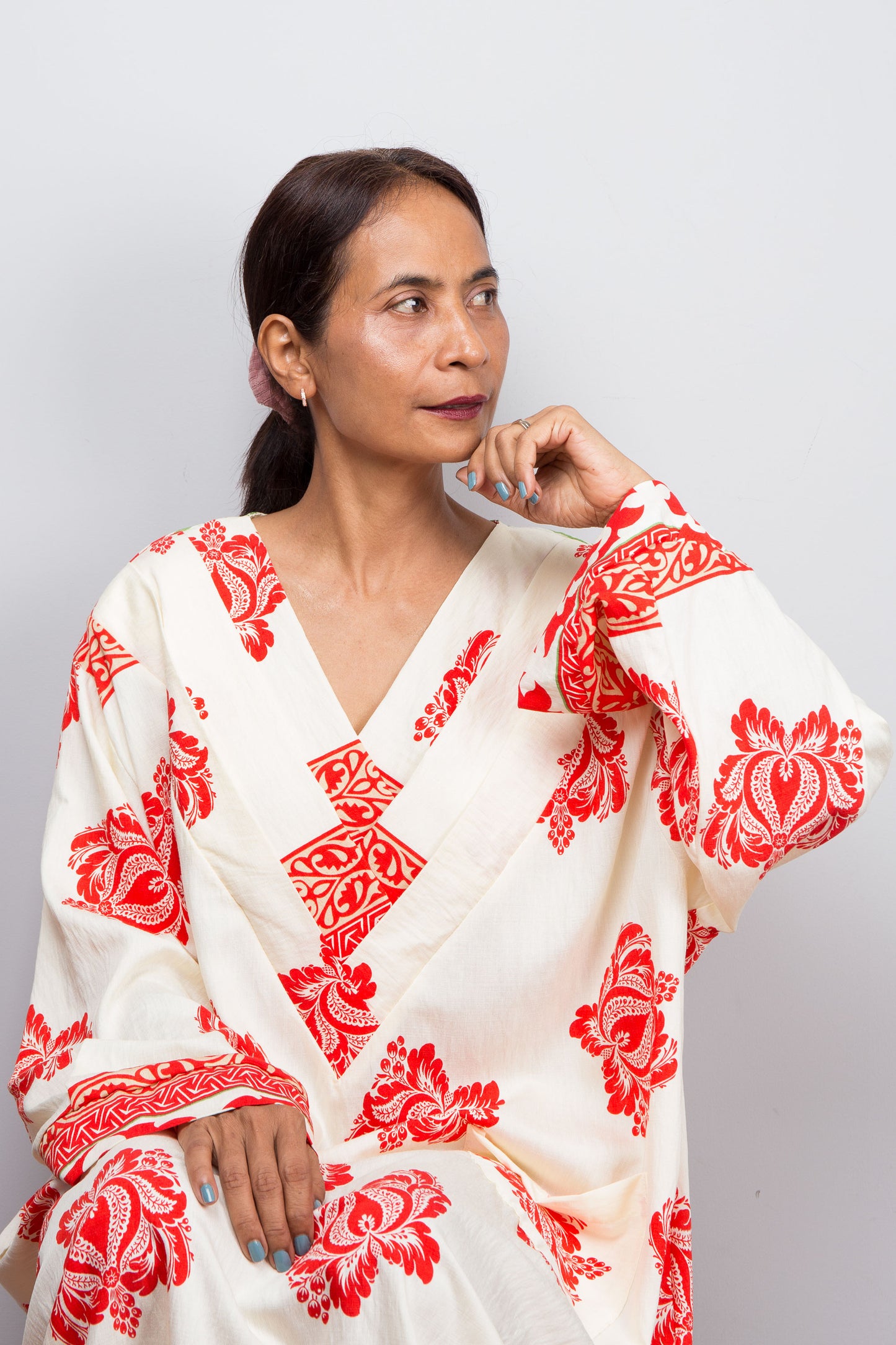 Woman wearing a white bohemian caftan with red patterns against a plain background